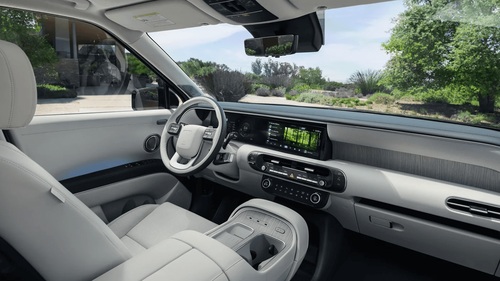 Front cabin view of the 2026 Hyundai Palisade showing the driver seat, steering wheel, wide dashboard display, center controls, and a large center console with cupholders and storage.