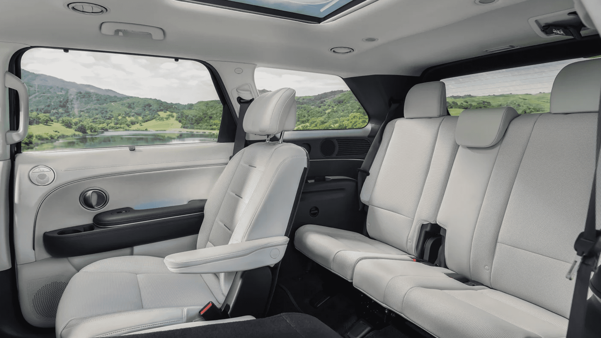 Third-row area of the 2026 Hyundai Palisade showing a light interior with a second-row seat in the foreground, a three-seat rear bench, panoramic sunroof, and scenic landscape outside.