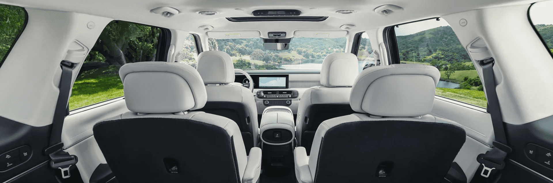 Rear cabin view of the 2026 Hyundai Palisade interior showing light seats across multiple rows, center console, dash screen, and wide side windows with green hills outside.