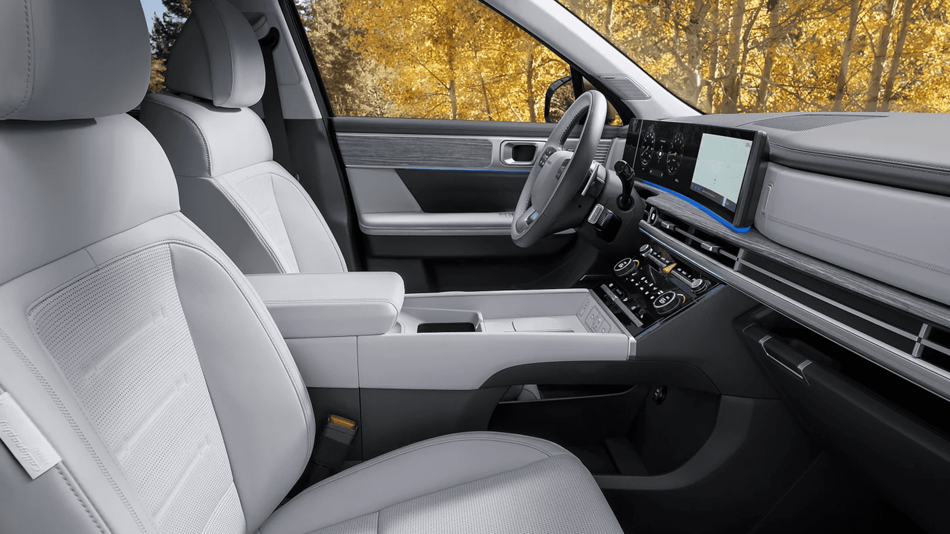 Front passenger side interior view of the 2026 Hyundai Santa Fe Hybrid with light upholstery, a wide dual screen display on the dash, horizontal air vents, layered trim on the door panel, and a large center console with storage.