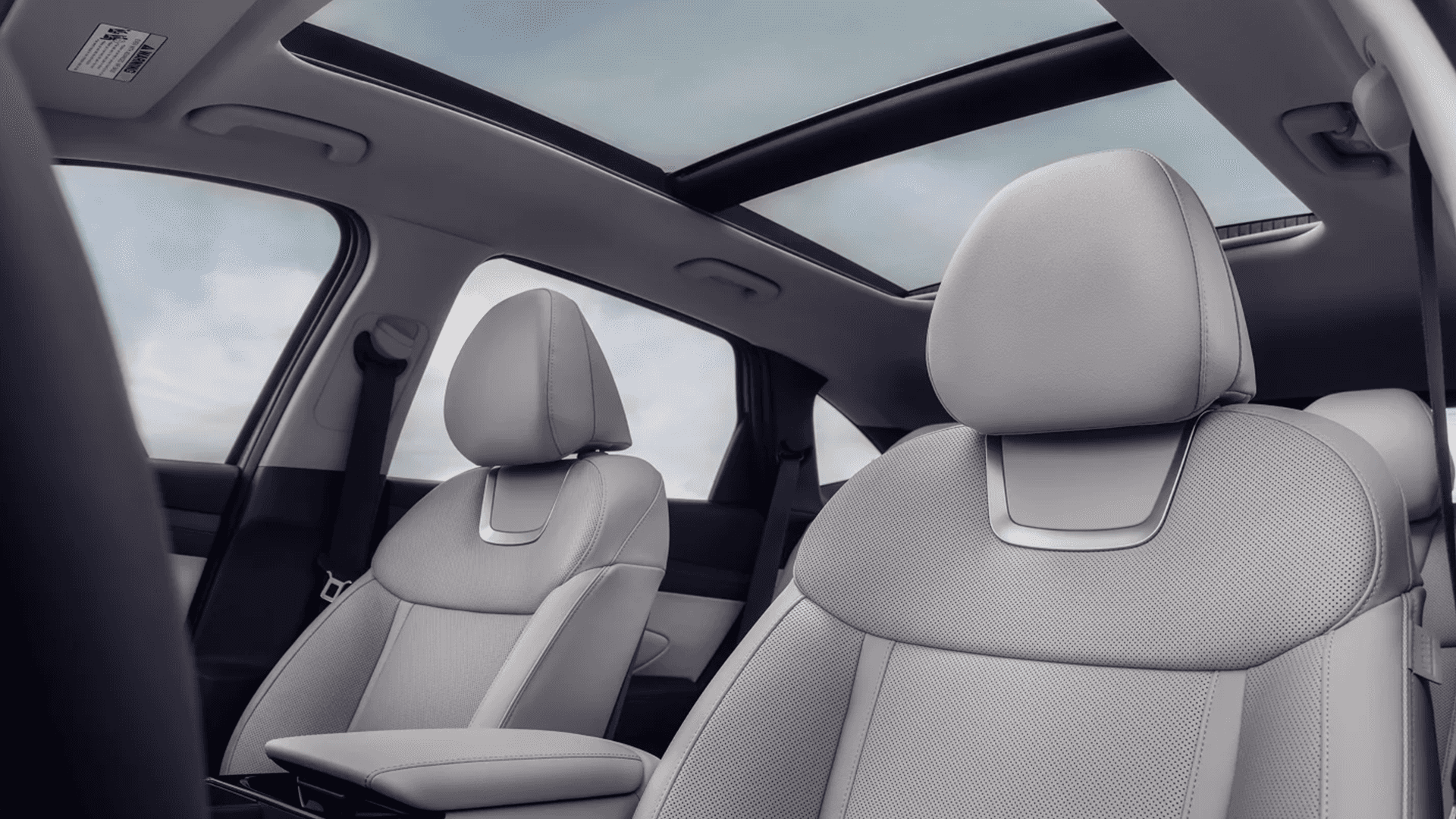 Front cabin view of a Hyundai Tucson with light gray perforated seats and headrests, center armrest, and a wide panoramic sunroof spanning over the front and rear seating area.