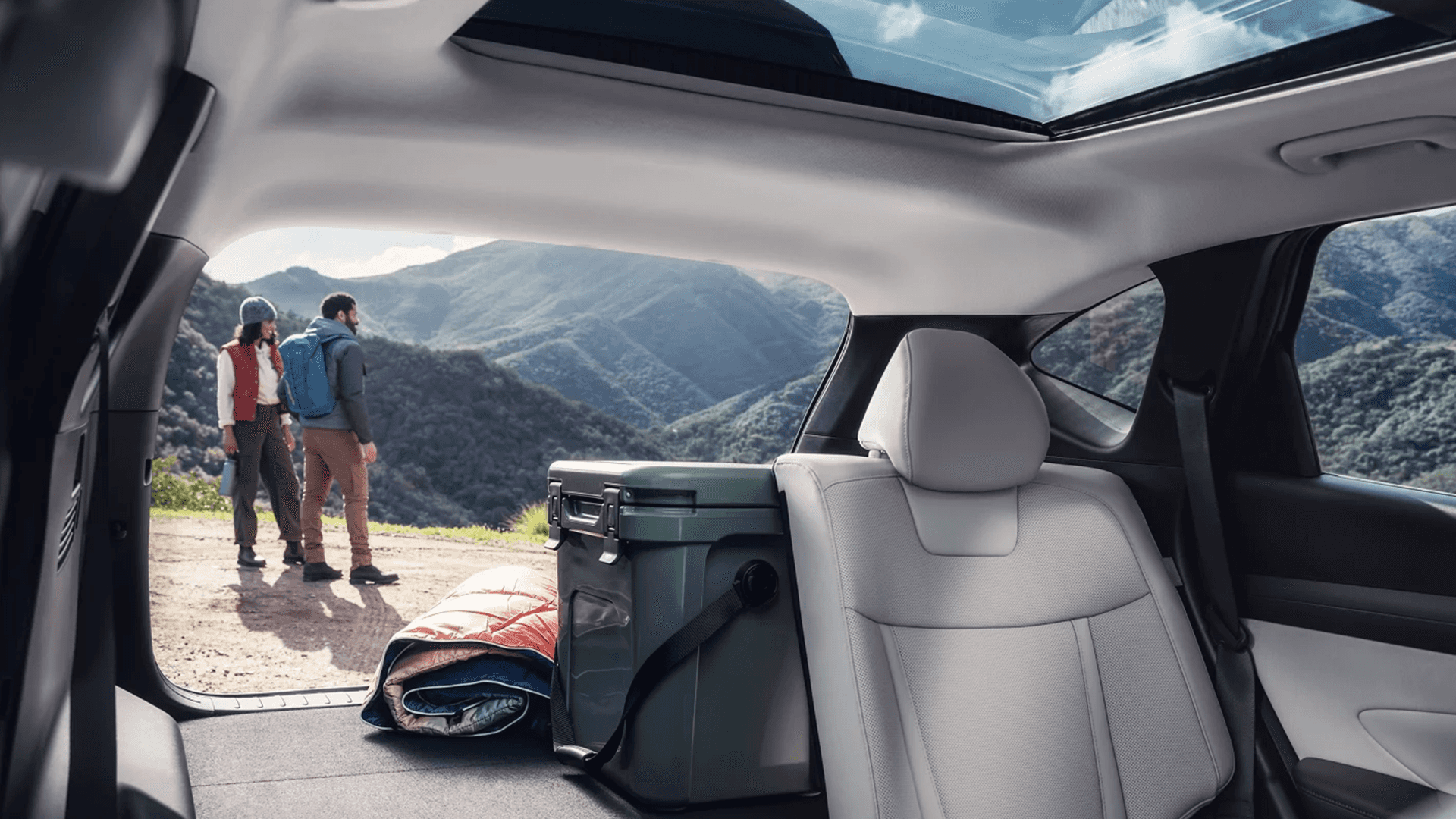 Rear cargo area of the 2026 Hyundai Tucson with a cooler and sleeping bag loaded behind the second row, viewed through the open liftgate with mountain scenery visible outside.