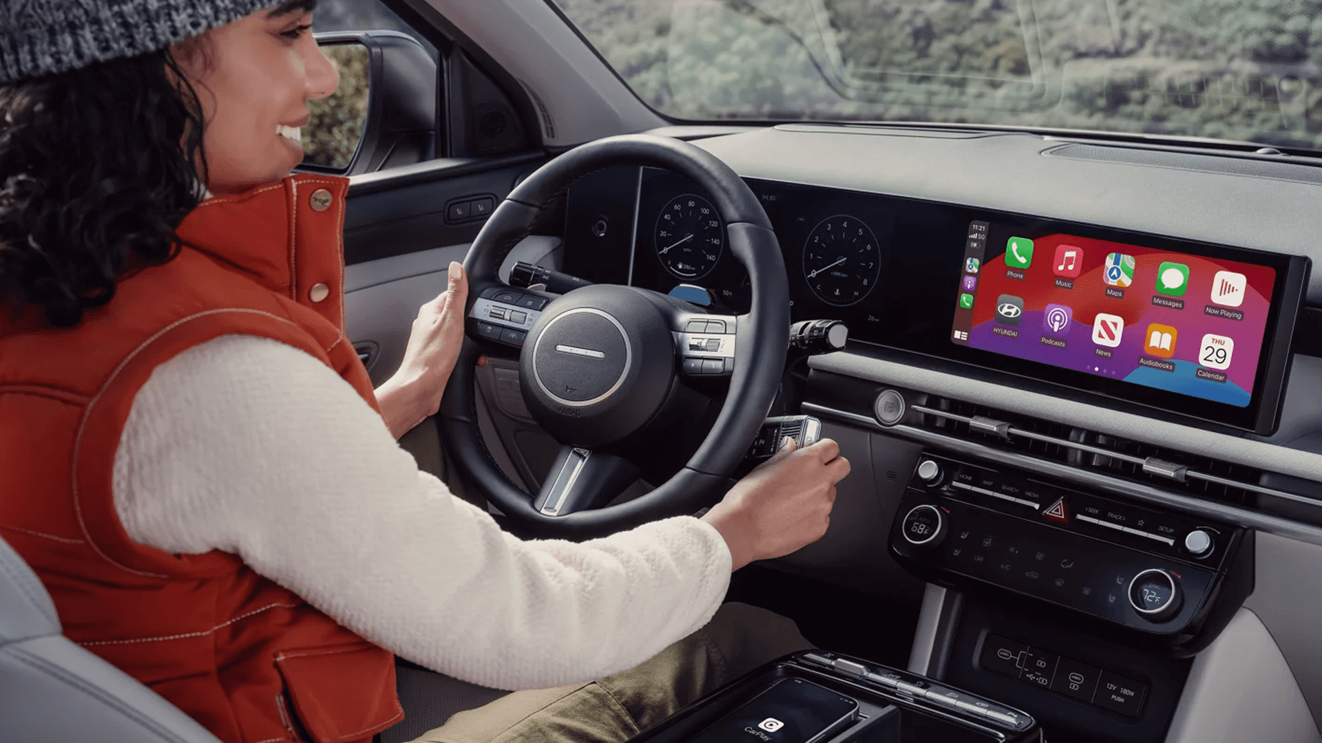 Driver using the 2026 Hyundai Tucson infotainment screen displaying Apple CarPlay, with the steering wheel, digital gauges, climate control panel, and center console visible in the foreground.