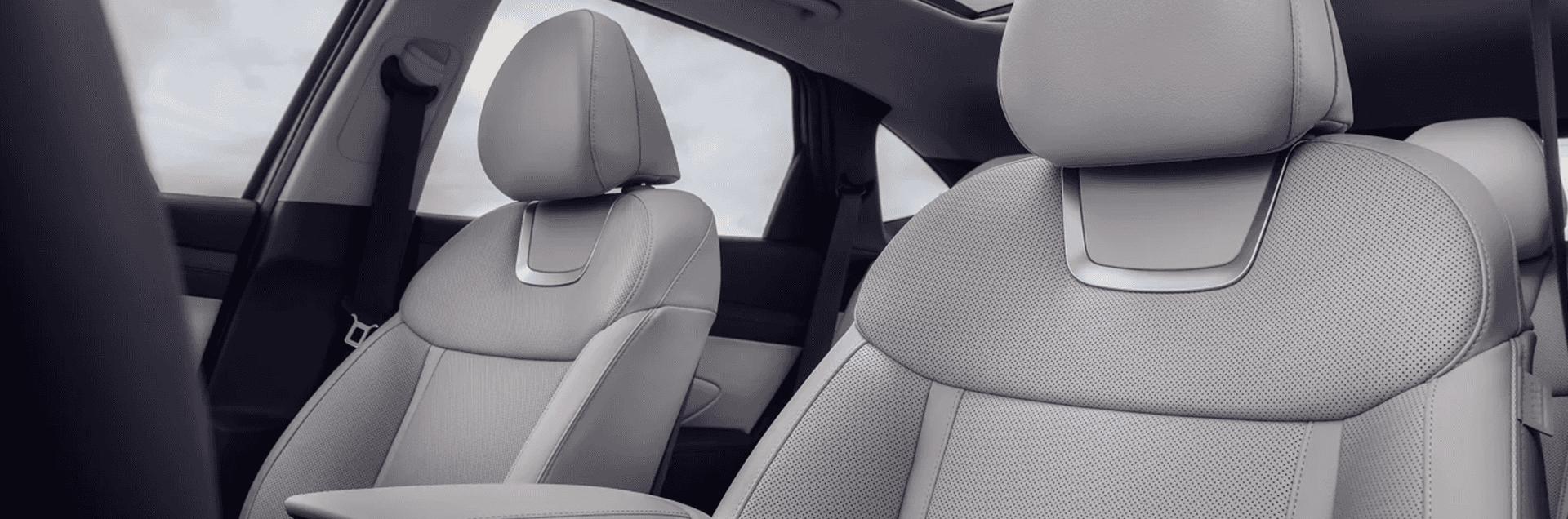 Front cabin view of the 2026 Hyundai Tucson showing light gray perforated front seats, headrests, and the upper cabin with a panoramic glass roof overhead.