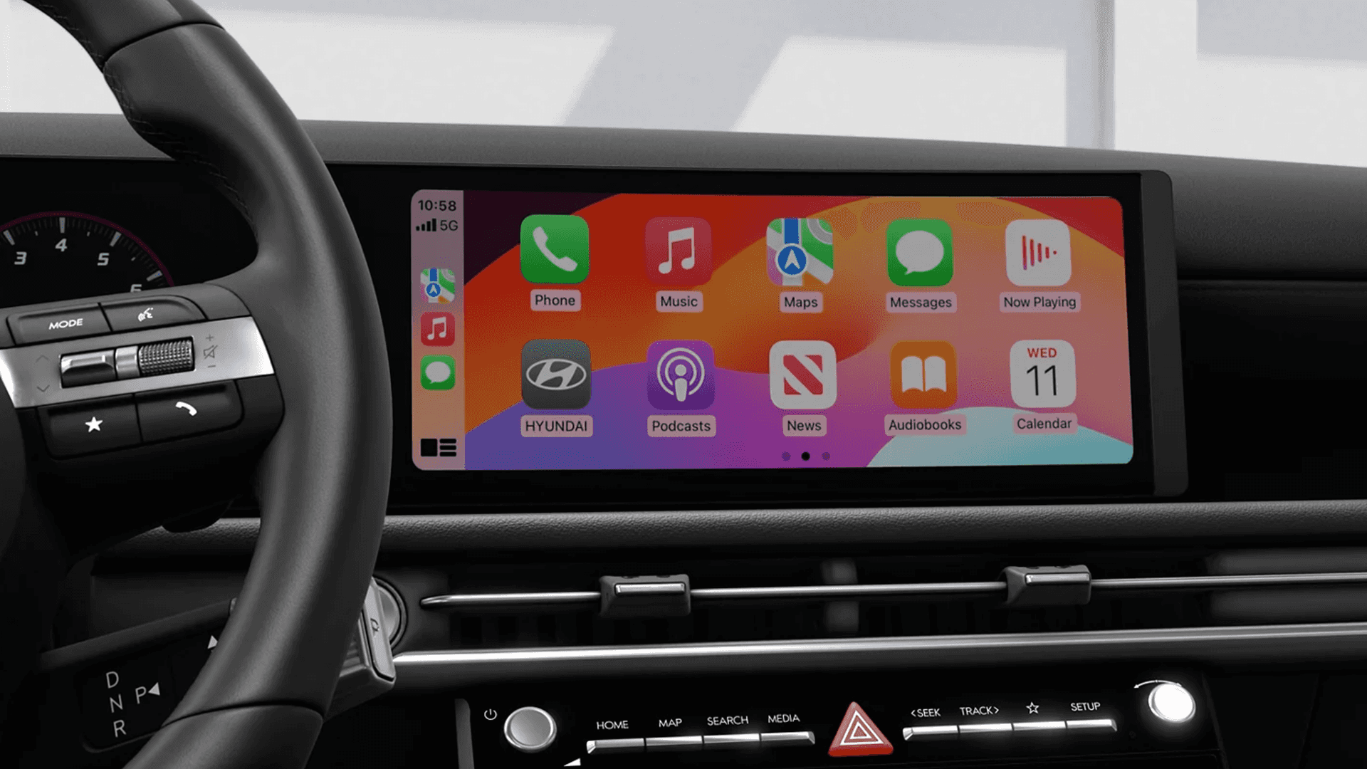 Close interior view of the Tucson center display showing Apple CarPlay icons across a wide touchscreen, with part of the steering wheel visible on the left.