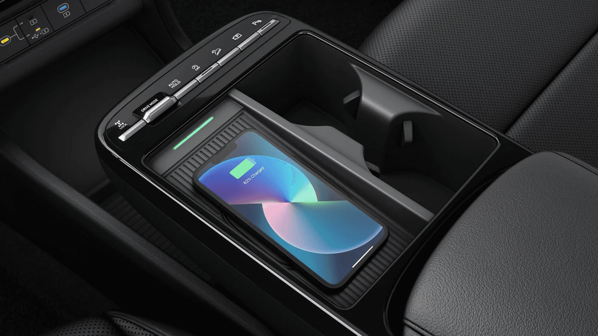 Center console view with a smartphone charging on a wireless charging pad next to dual cupholders and drive mode style buttons.