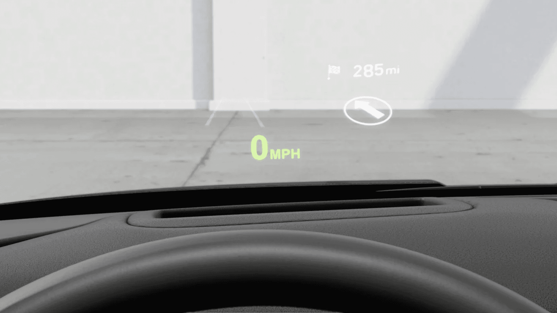 Driver perspective showing a head up display projecting speed at 0 mph and navigation guidance onto the windshield above the steering wheel.