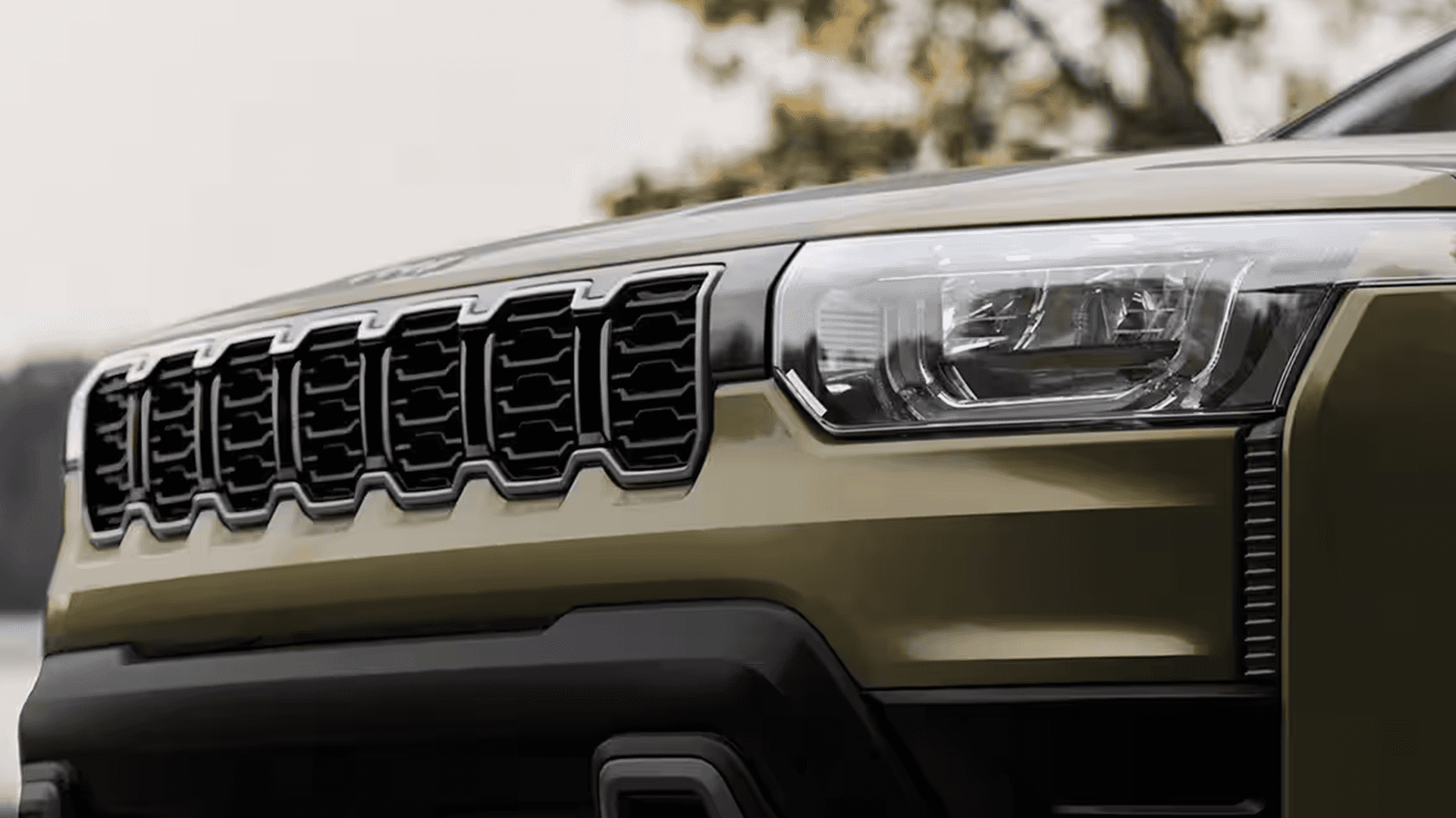 Close-up of the Jeep Cherokee front fascia, focusing on the seven-slot grille pattern and the right headlamp assembly above a black lower bumper.