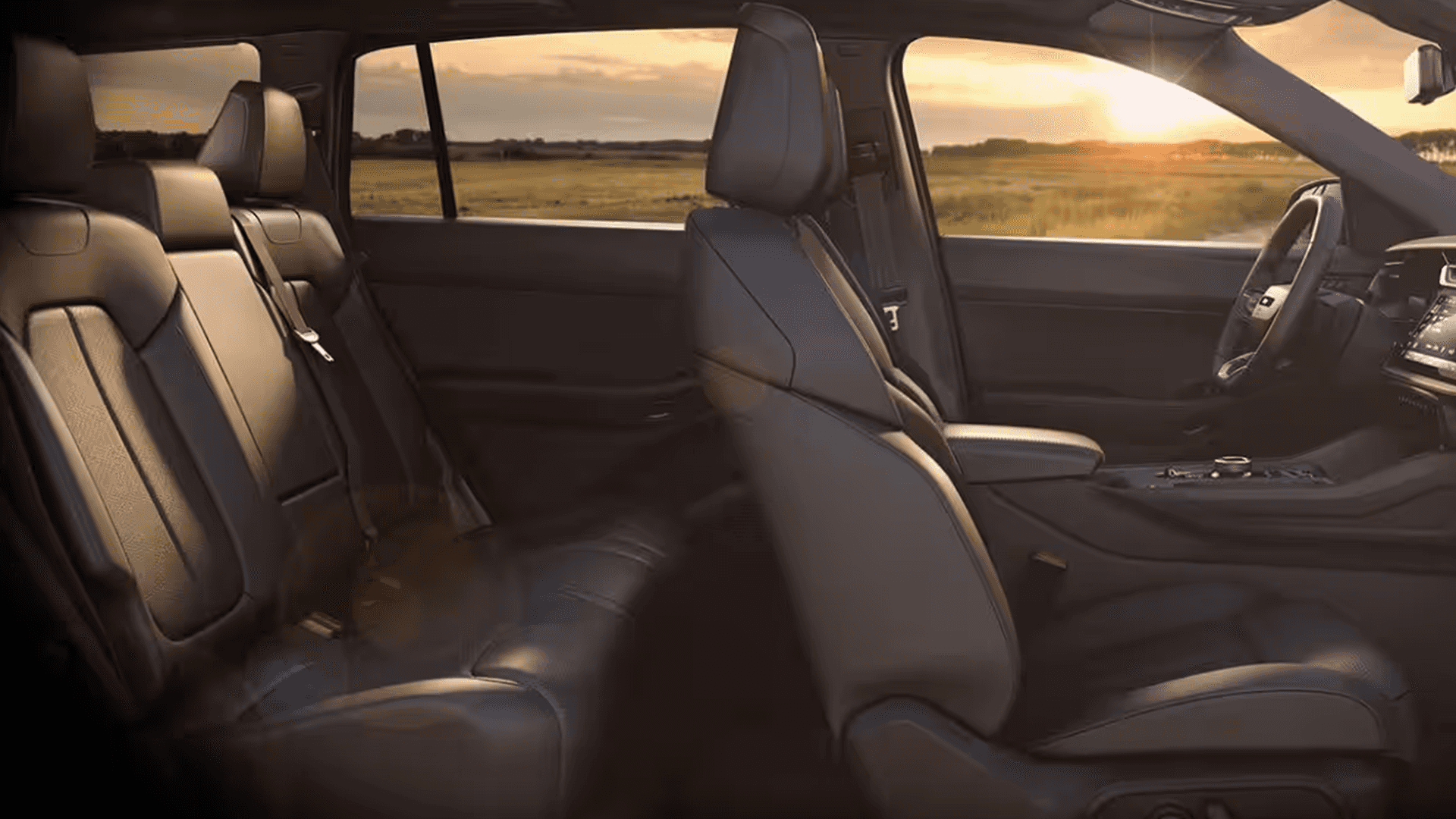 Side view across the 2026 Jeep Cherokee cabin showing the rear bench seat, front seats, center console, and dashboard with a sunset landscape visible through the windows.