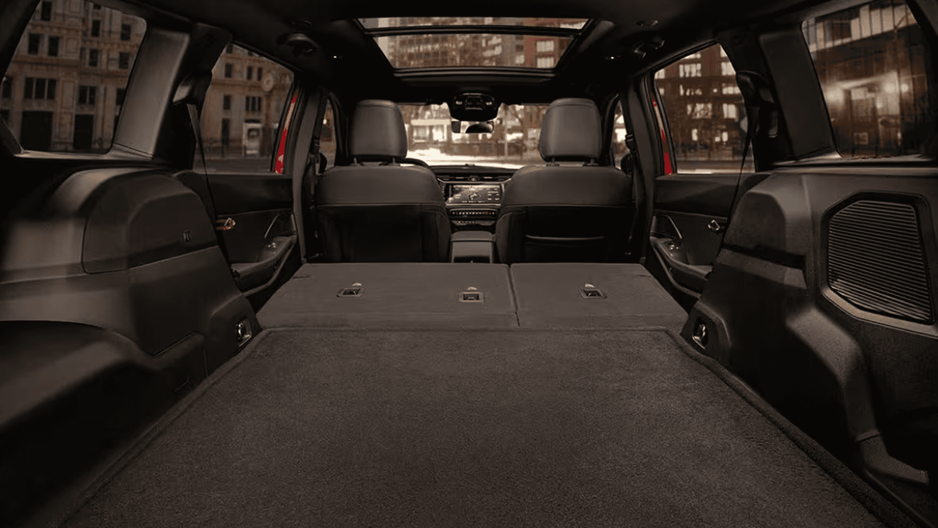 Rear to front view of the 2026 Jeep Cherokee with the second row folded flat, showing a long cargo floor, rear speaker grilles, and the dashboard visible ahead under a panoramic roof.