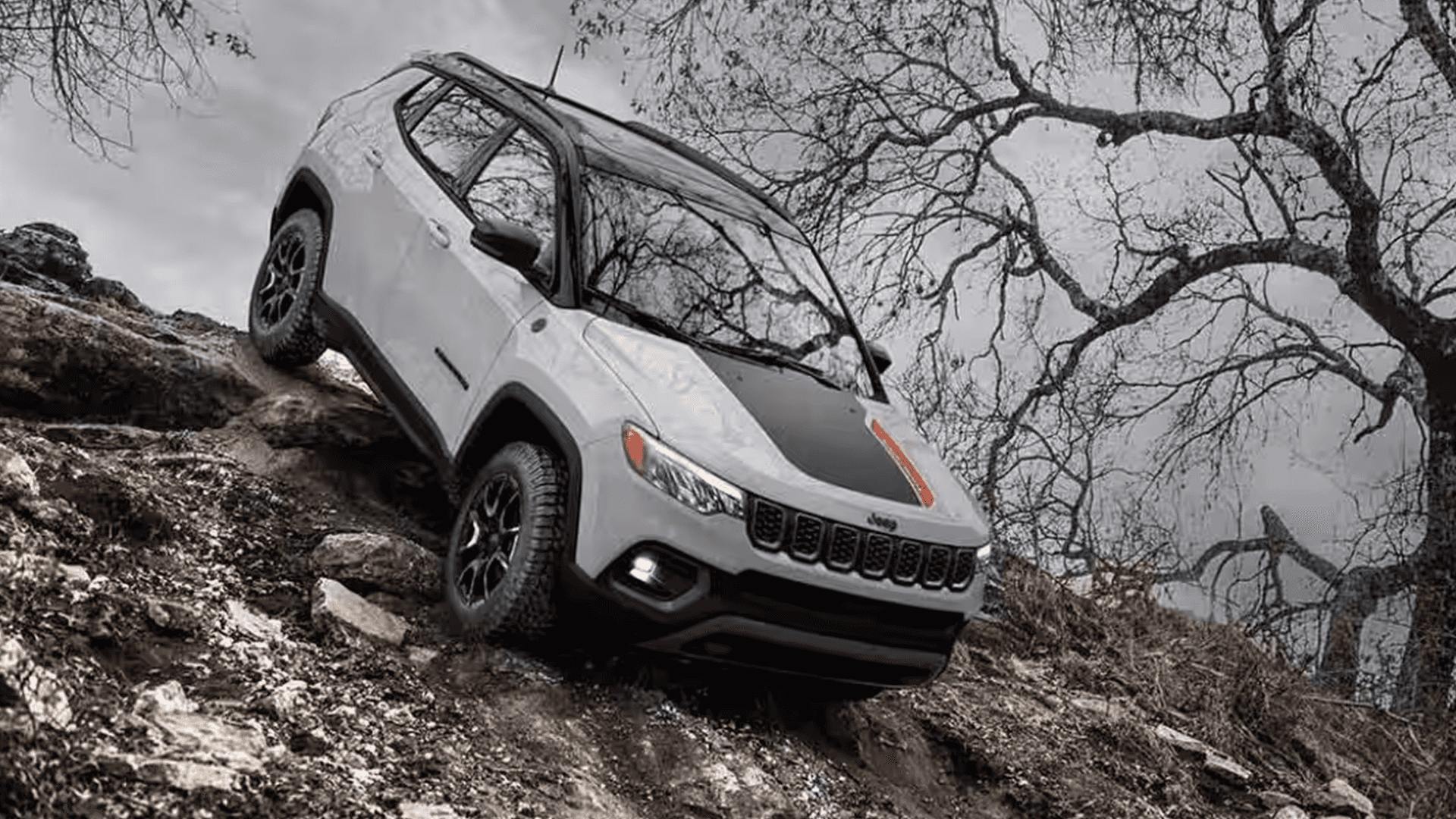 White Jeep Compass Trailhawk climbing over rocky terrain on a steep off-road trail.
