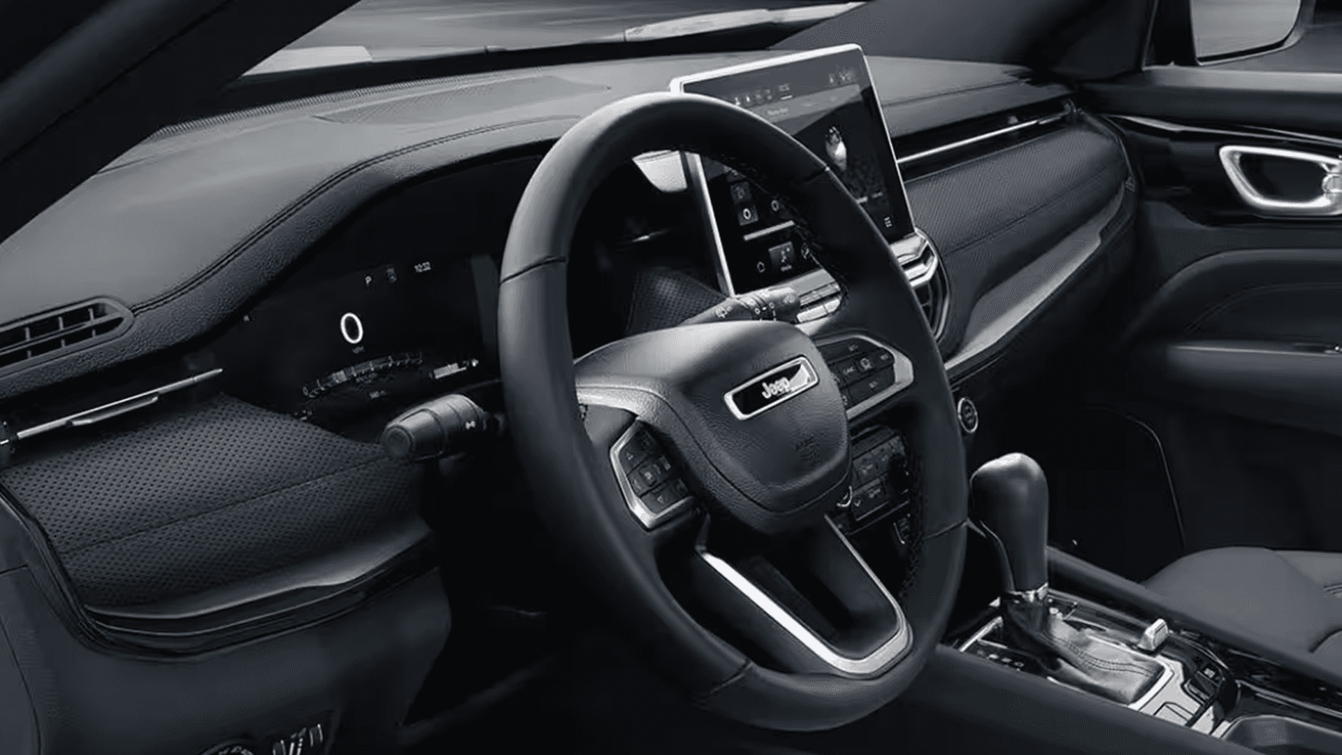 Jeep Compass driver area showing steering wheel, dashboard trim, digital cluster, center touchscreen, and console shifter.