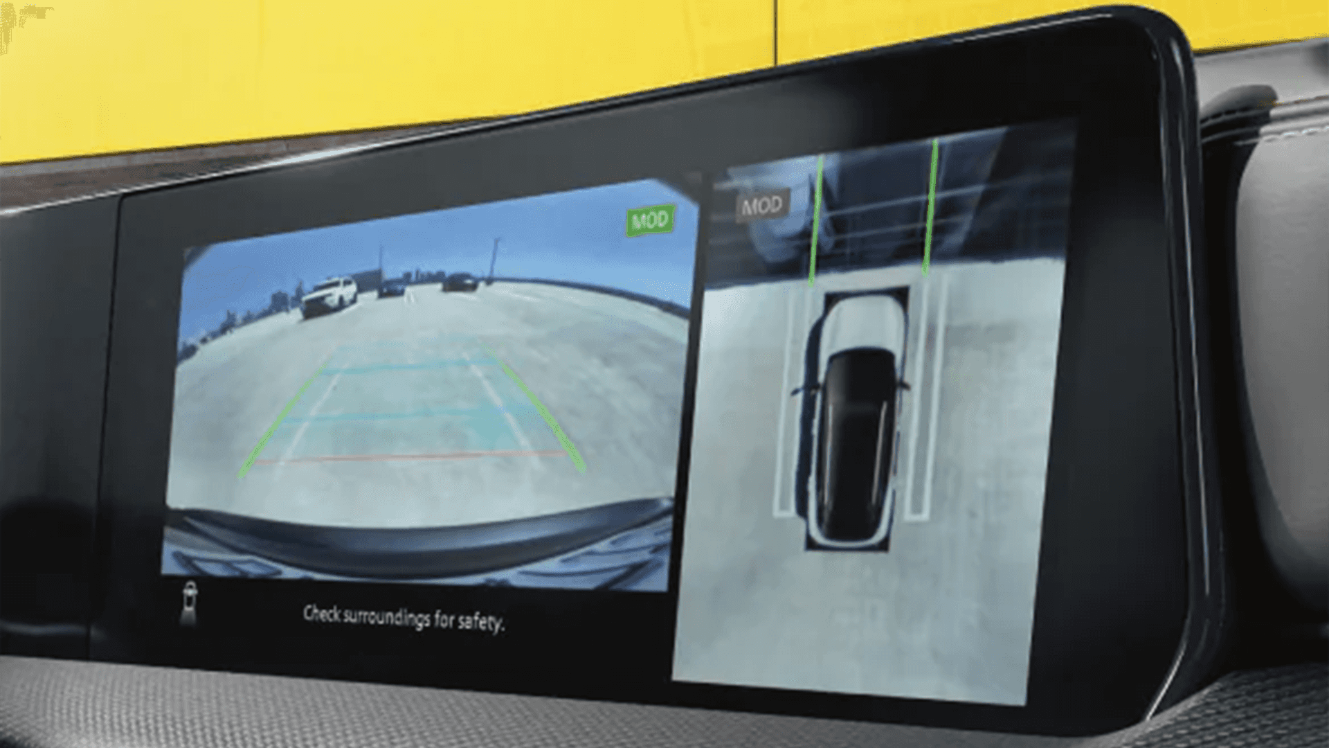 Close up of an in dash screen showing a rear camera view and a top down surround view parking display with guidance lines, illustrating driver assist visibility while maneuvering