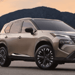 Beige Nissan Rogue parked in a driveway near a modern home at sunset with mountains in the background