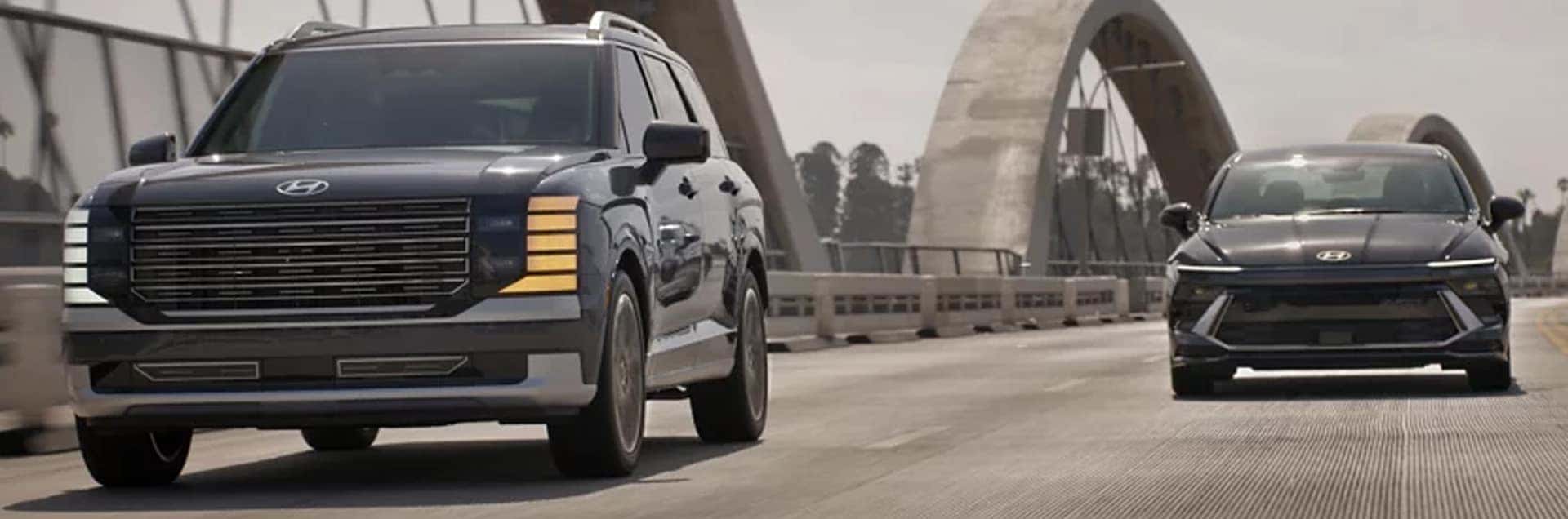 2026 Hyundai Palisade Hybrid driving on a bridge next to a Hyundai hybrid sedan, showcasing fuel efficiency and updated exterior design
