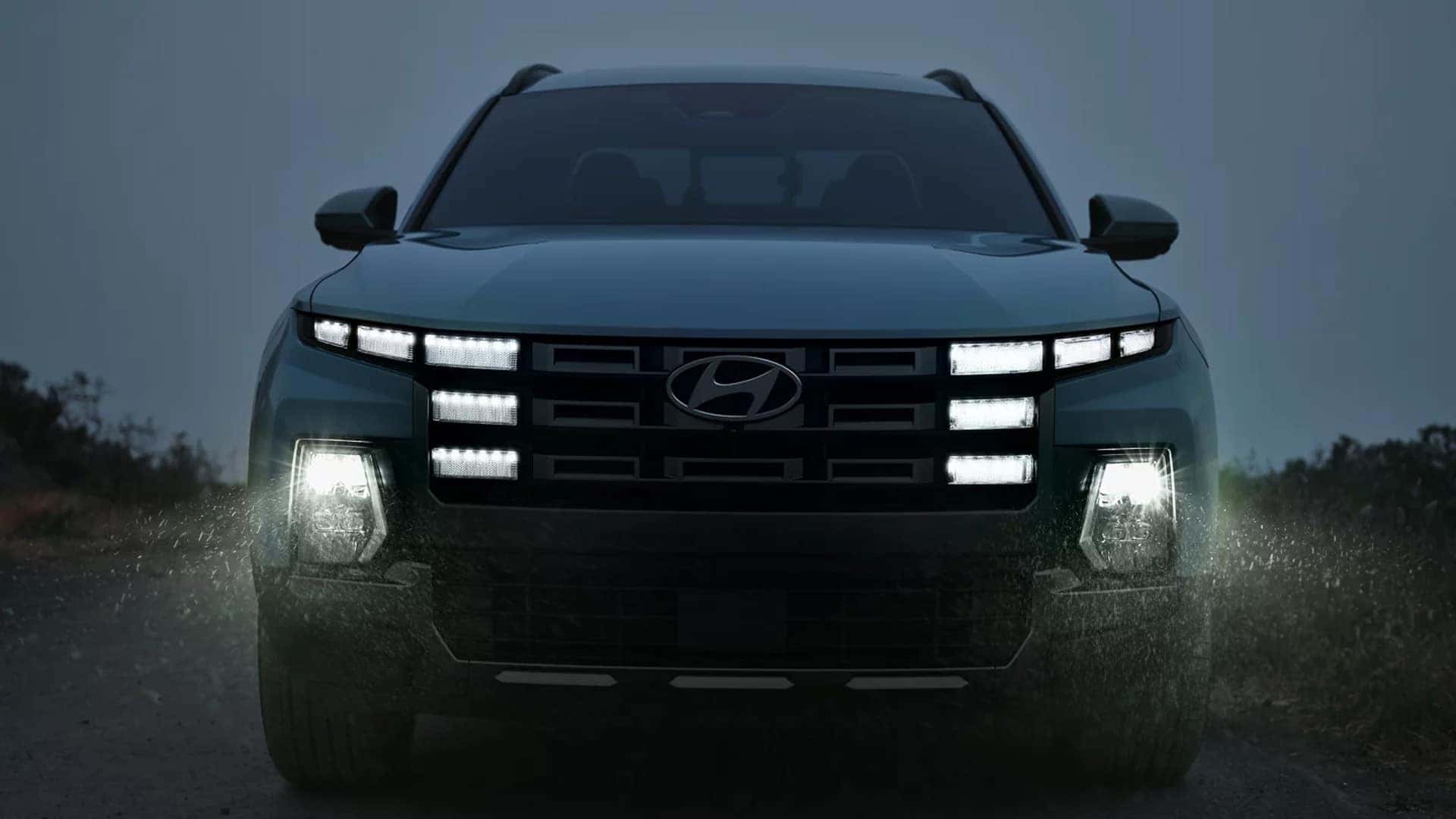 Front view of the 2026 Hyundai Santa Cruz at night with LED headlights and illuminated grille lighting signature in rainy conditions.
