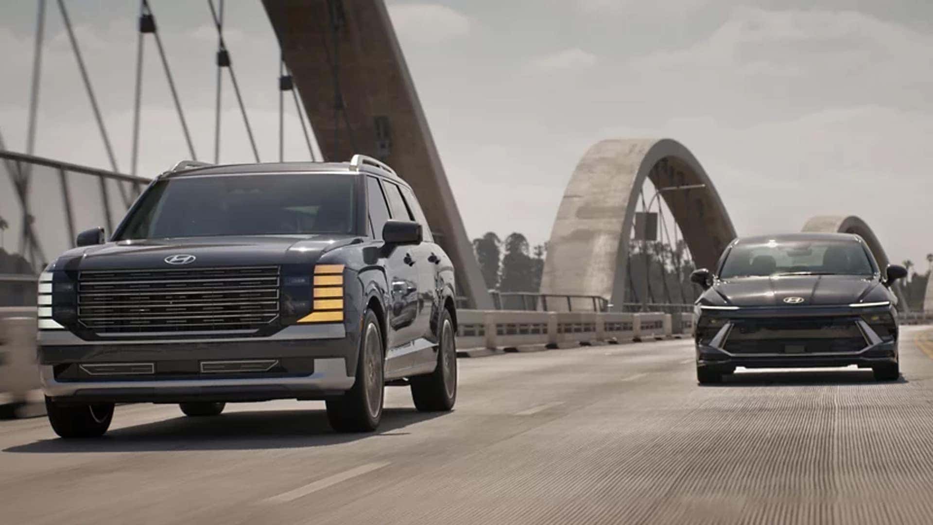 2026 Hyundai Palisade Hybrid driving on a city bridge alongside a Hyundai sedan, highlighting hybrid performance and modern exterior styling