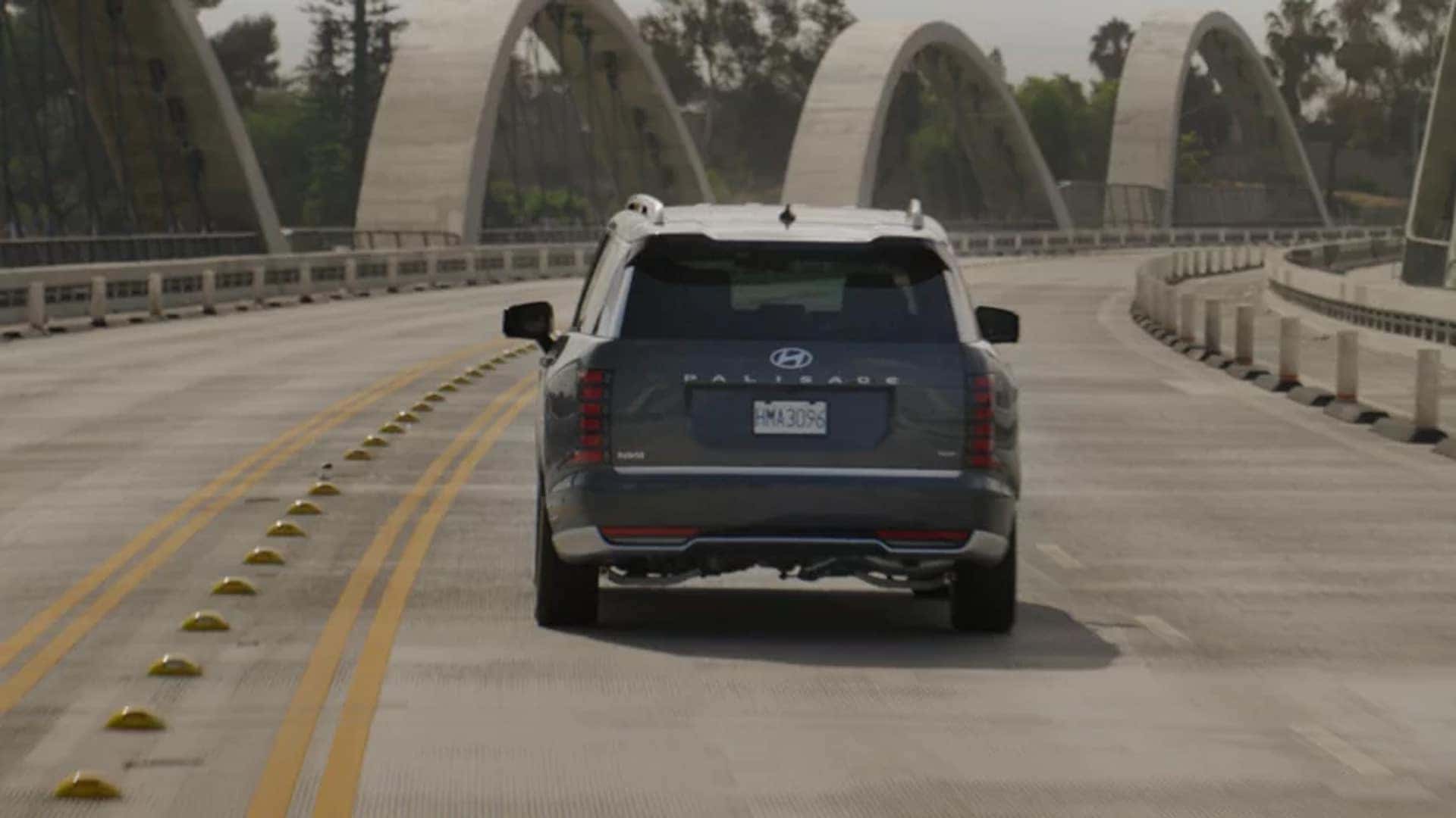 Rear view of a 2026 Hyundai Palisade Hybrid driving on a roadway, illustrating regenerative braking and hybrid energy recovery during deceleration.