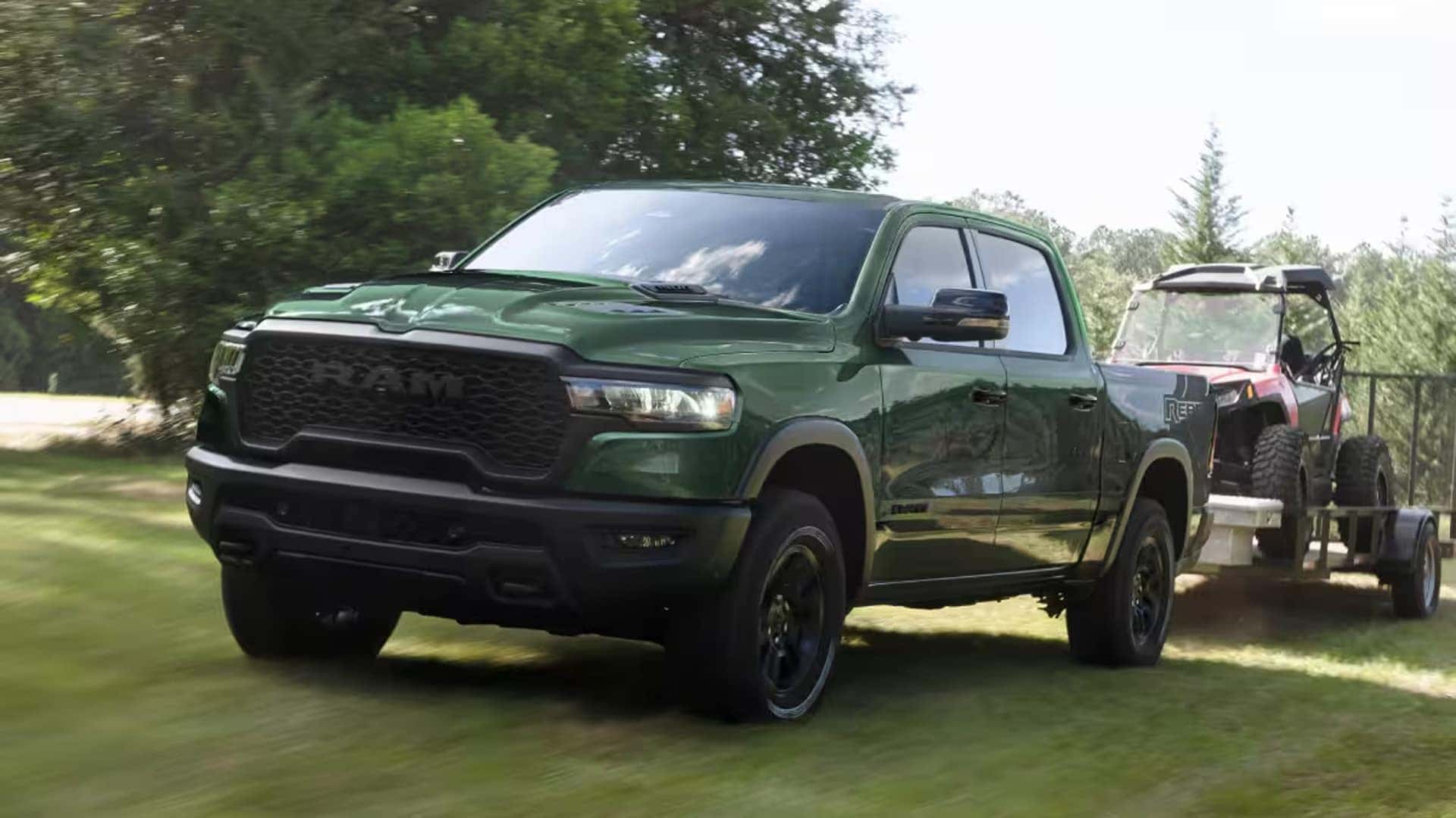 2026 Ram 1500 towing an off road side by side vehicle on a trailer through a grassy area