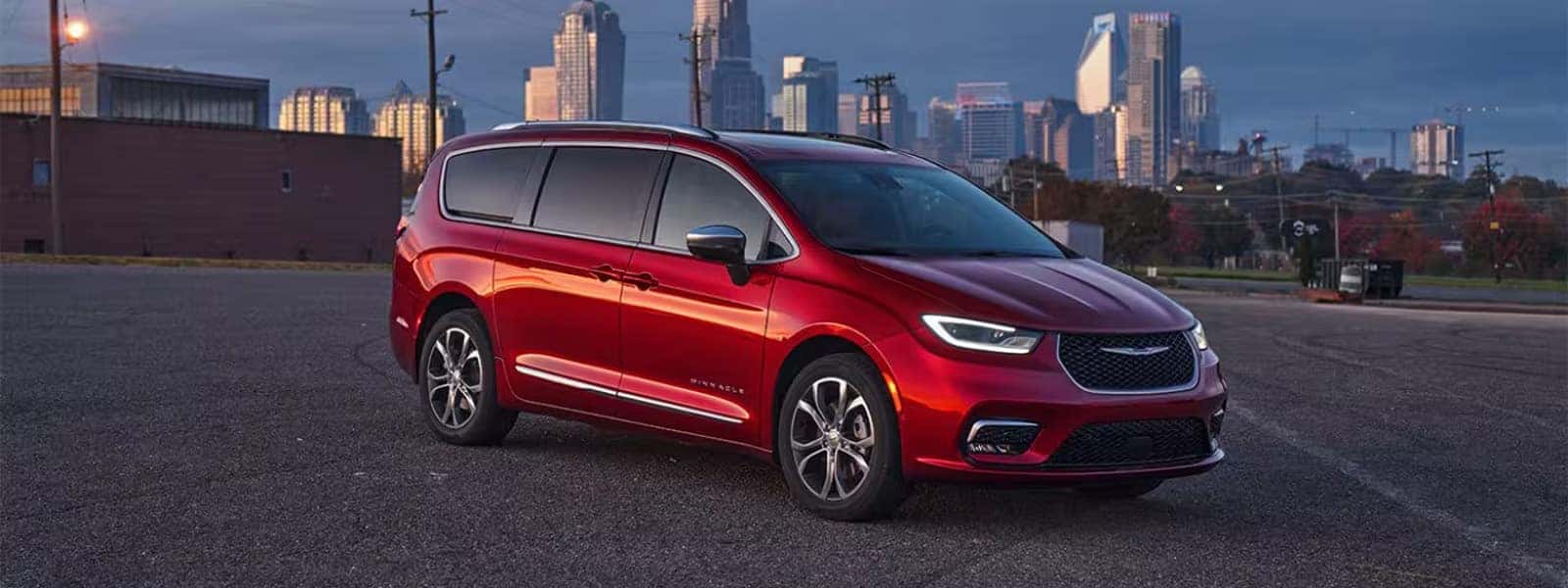 Red 2026 Chrysler Pacifica Pinnacle parked in front of a city skyline, front three quarter exterior view