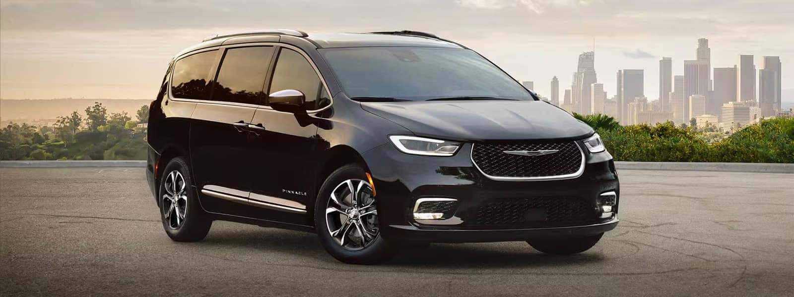 2026 Chrysler Pacifica minivan in black, front three quarter view with city skyline in the background