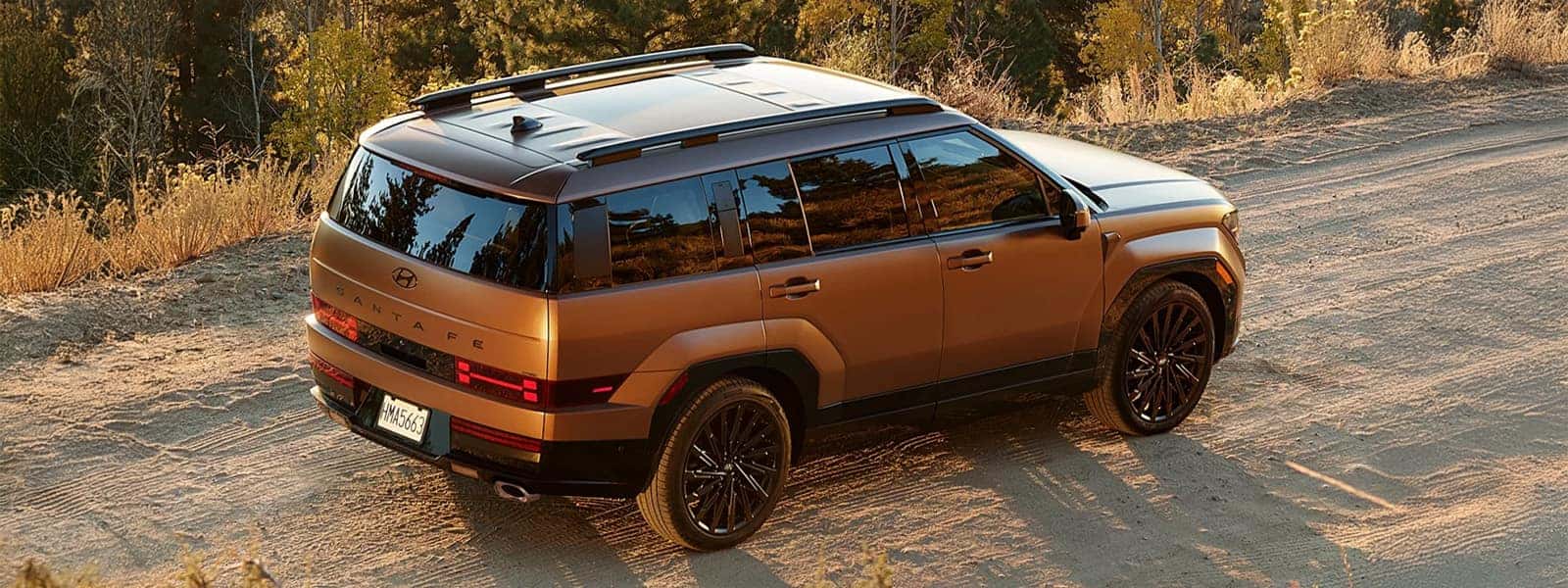 2026 Hyundai Santa Fe driving on a dirt road with a boxy SUV profile, roof rails, and rugged exterior styling shown in a natural landscape