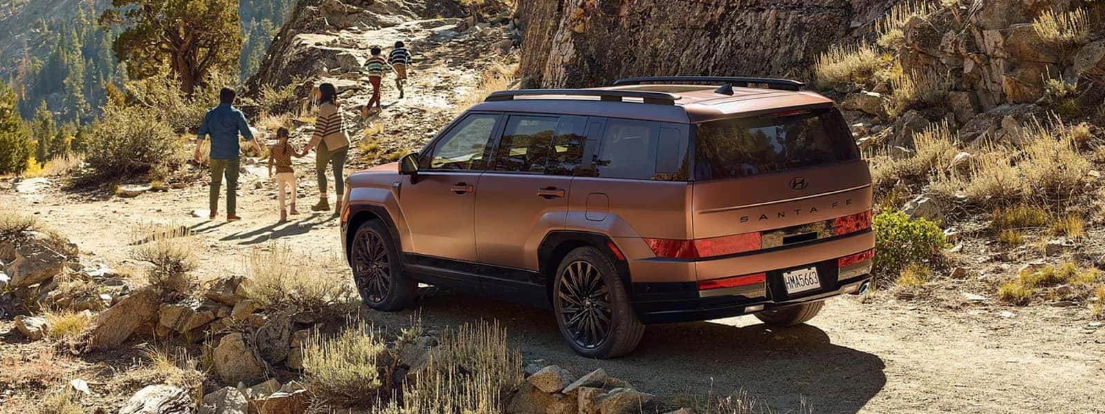 2026 Hyundai Santa Fe driving on a rocky mountain trail with hikers nearby, rear three quarter view