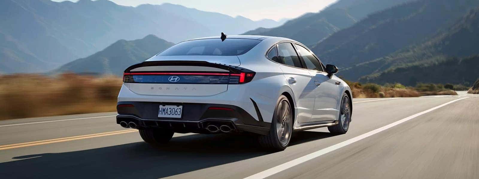 Rear three quarter view of a 2026 Hyundai Sonata Hybrid driving on a mountain road