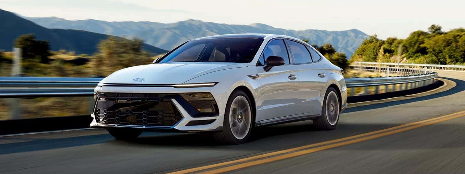 2026 Hyundai Sonata driving on a highway with mountains in the background, front three quarter view
