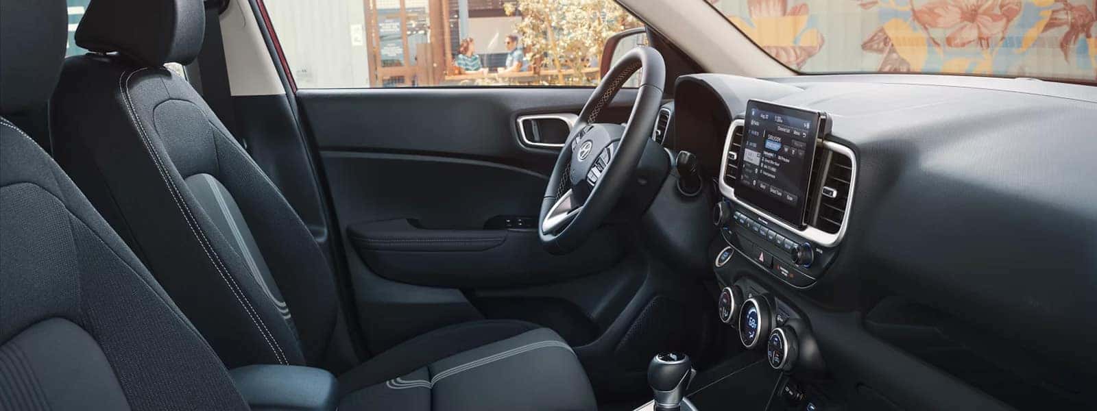 Front seats and dashboard of the 2026 Hyundai Venue interior with touchscreen display, steering wheel, and center climate controls.