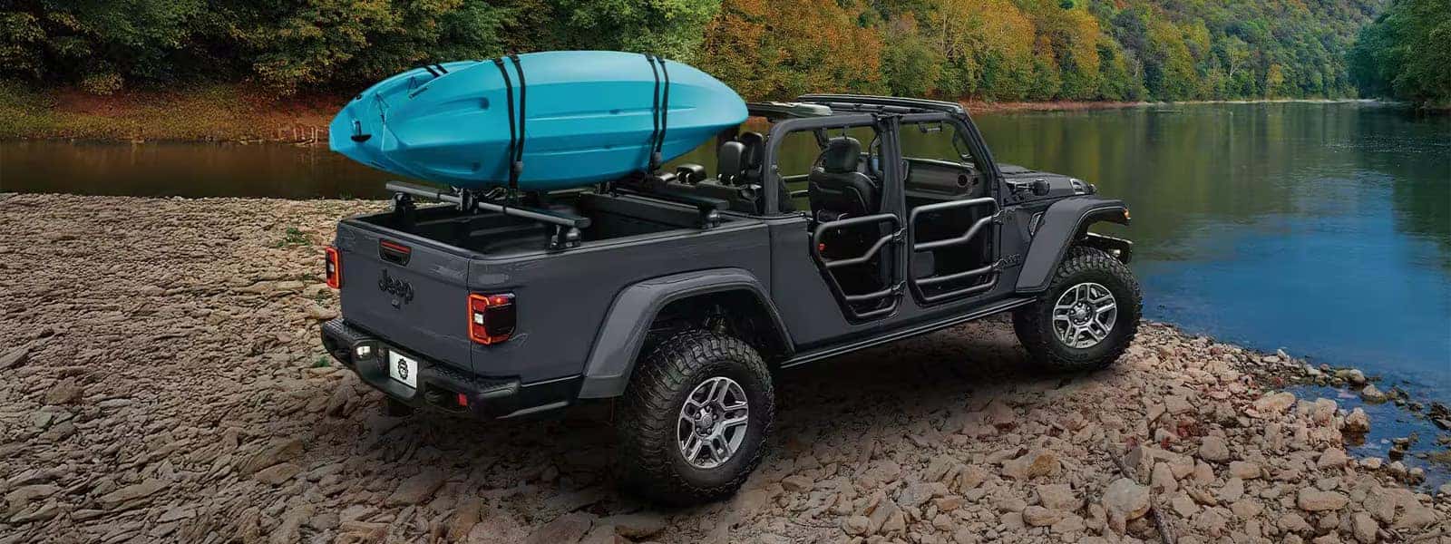 2026 Jeep Gladiator parked on a rocky lakeshore with open-air doors and kayaks secured in the truck bed
