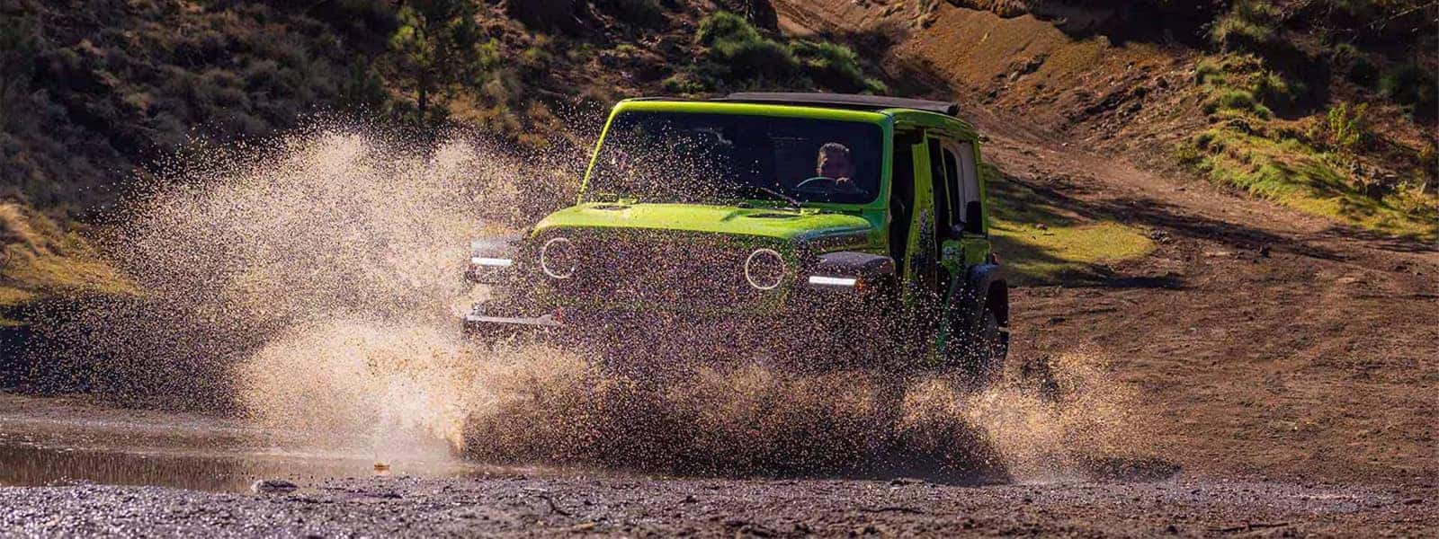 2026 Jeep Wrangler in bright green splashing through a shallow creek on an off-road trail.