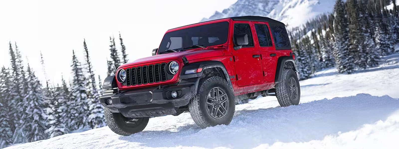 2026 Jeep Wrangler four-door driving through snow in the mountains with hardtop roof and rugged all-terrain tires