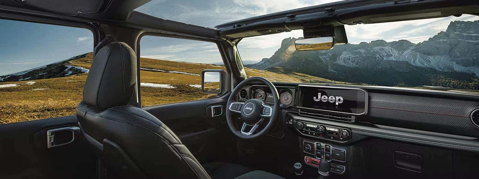 Driver cockpit of the 2026 Jeep Wrangler interior with 12.3-inch touchscreen, steering wheel controls, and open roof view of mountains