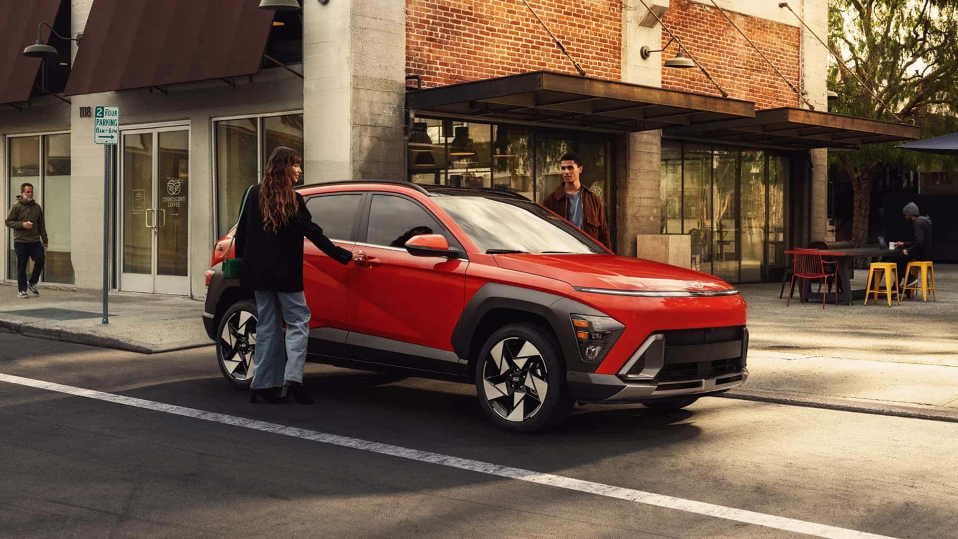 Red 2026 Hyundai Kona parked on a city street near storefronts, highlighting exterior design, roof rails, and modern compact SUV styling.