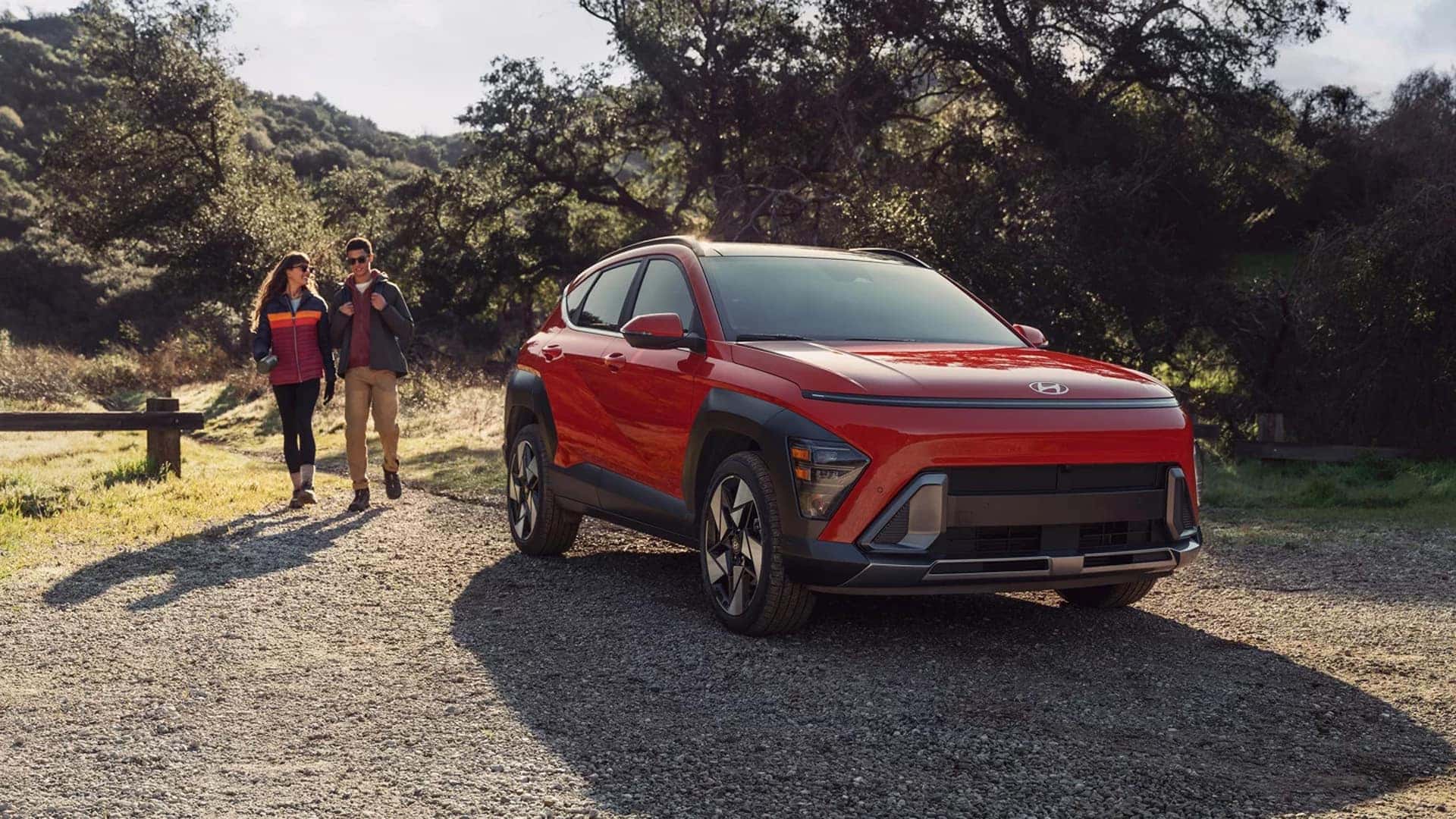 Front three quarter view of a red 2026 Hyundai Kona on a gravel road, highlighting modern lighting design, sculpted body lines, and compact SUV proportions