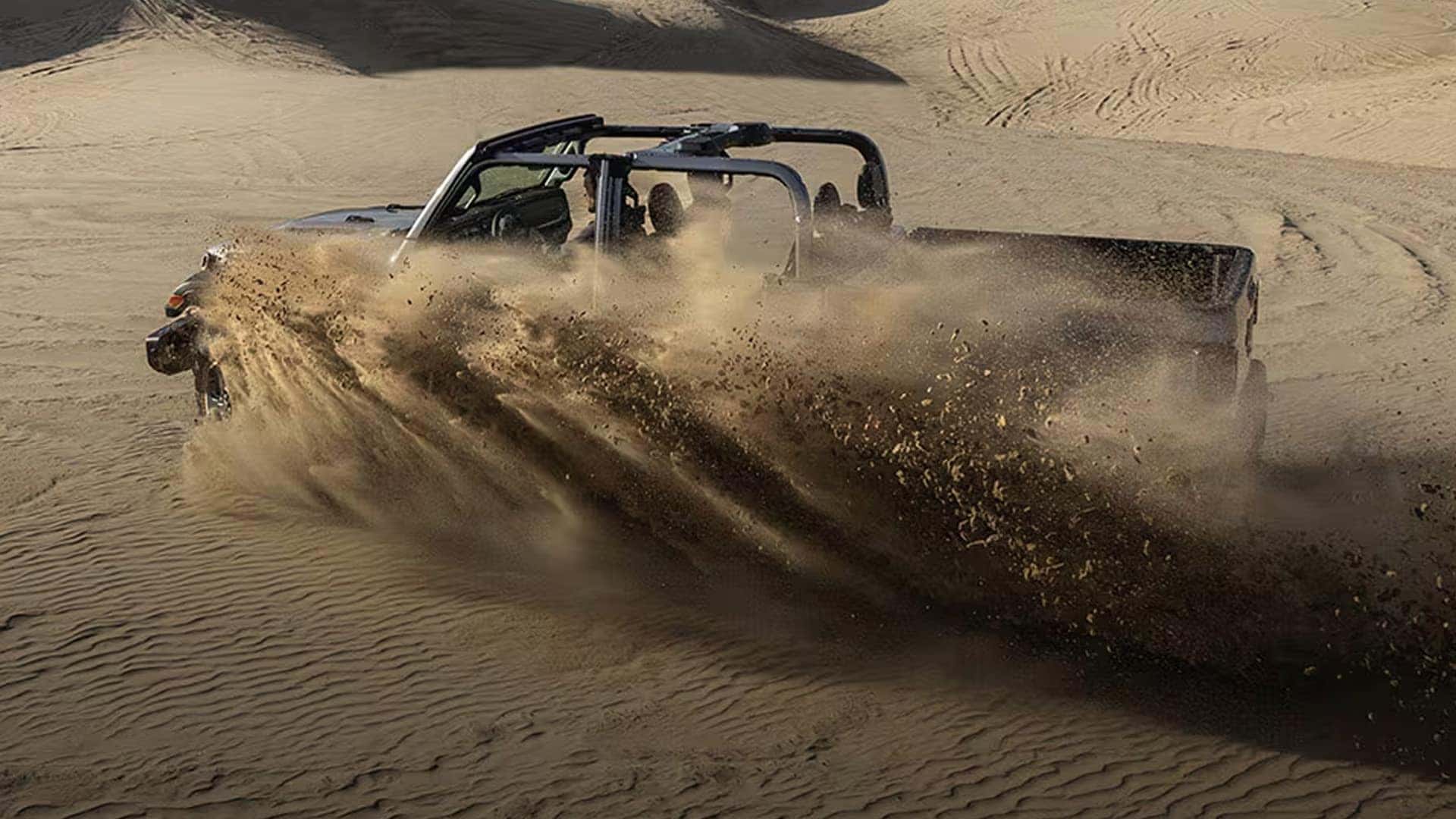 2026 Jeep Gladiator driving through desert dunes with open-air roof setup and sand spraying behind the truck.