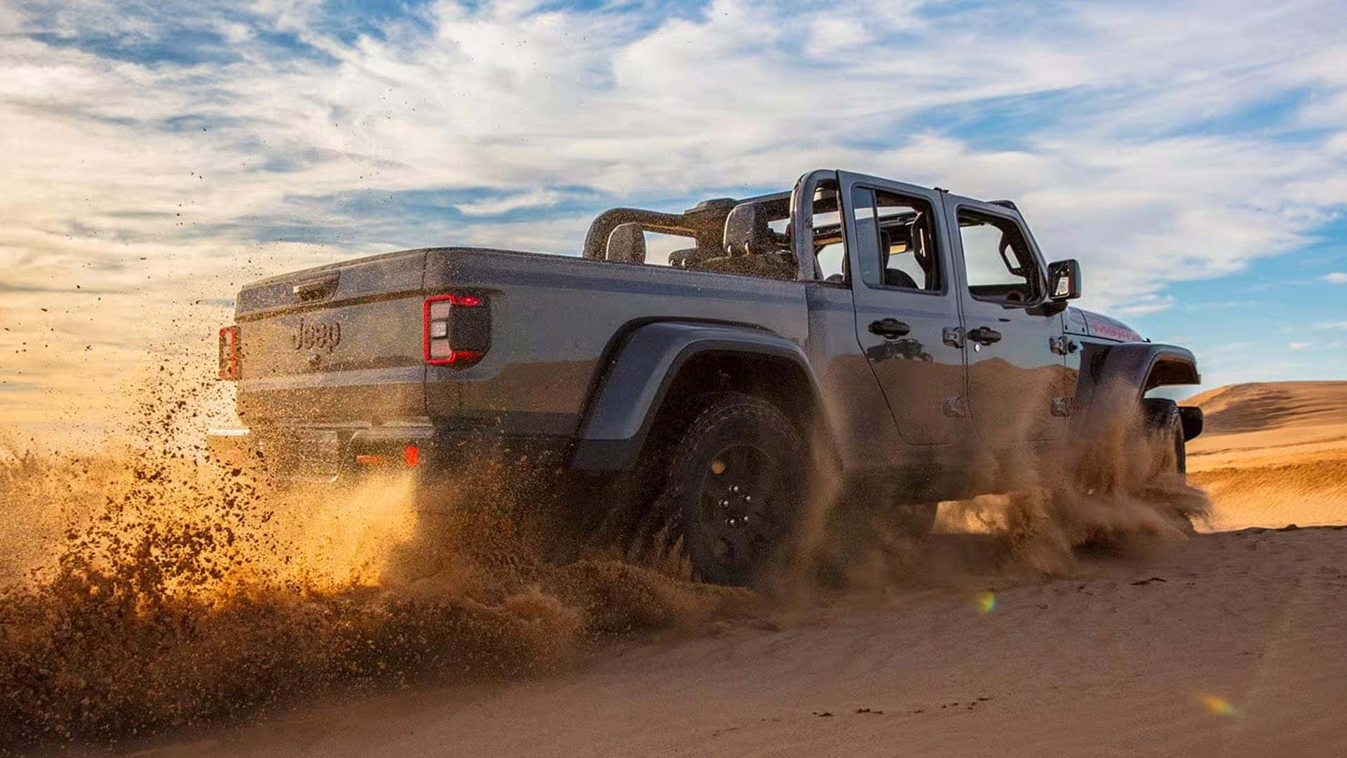 Rear three-quarter view of a 2026 Jeep Gladiator driving through sand, highlighting the truck bed and off-road traction