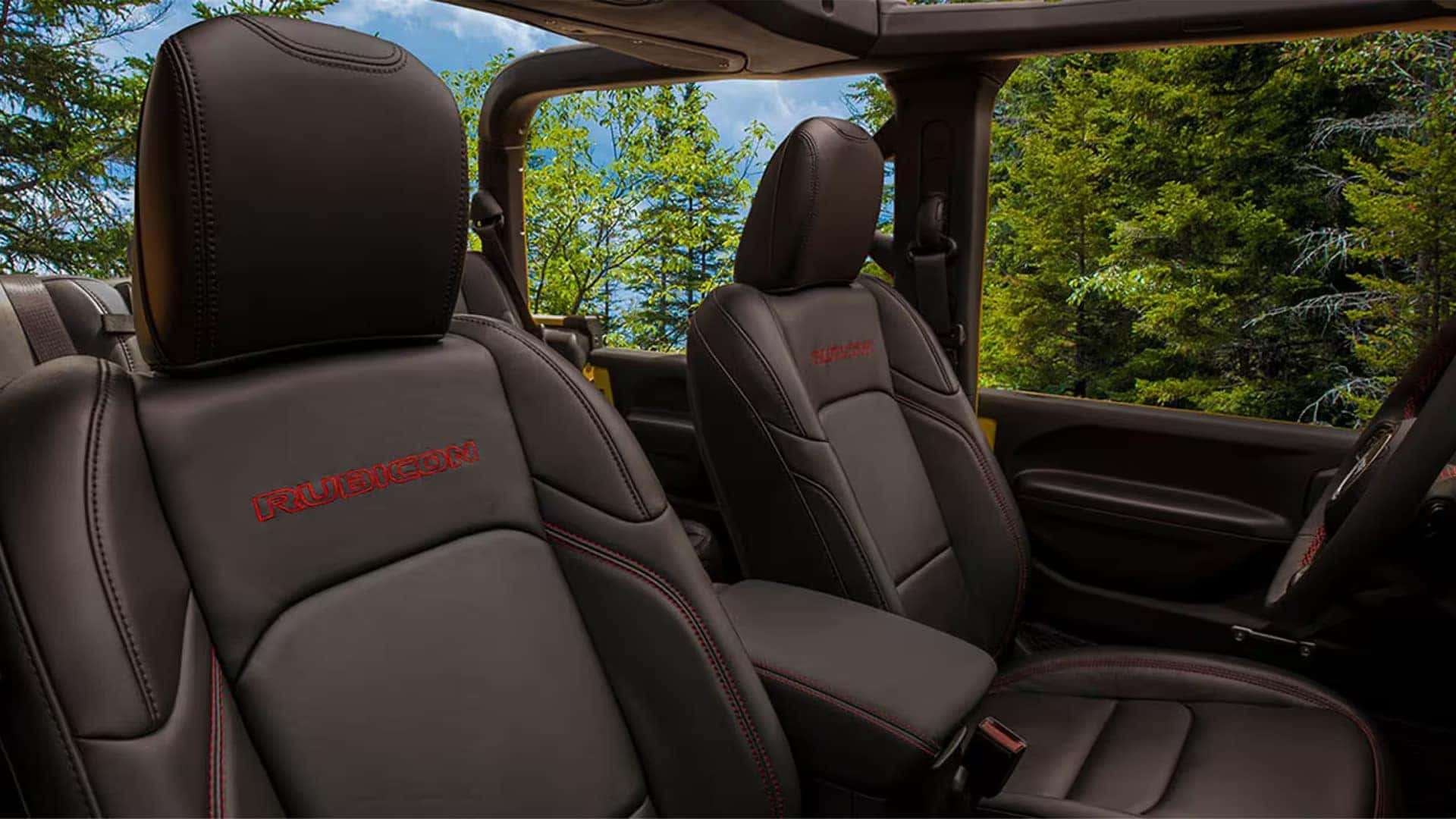 2026 Jeep Gladiator Rubicon interior with leather-trimmed front seats and open-air roof view of trees