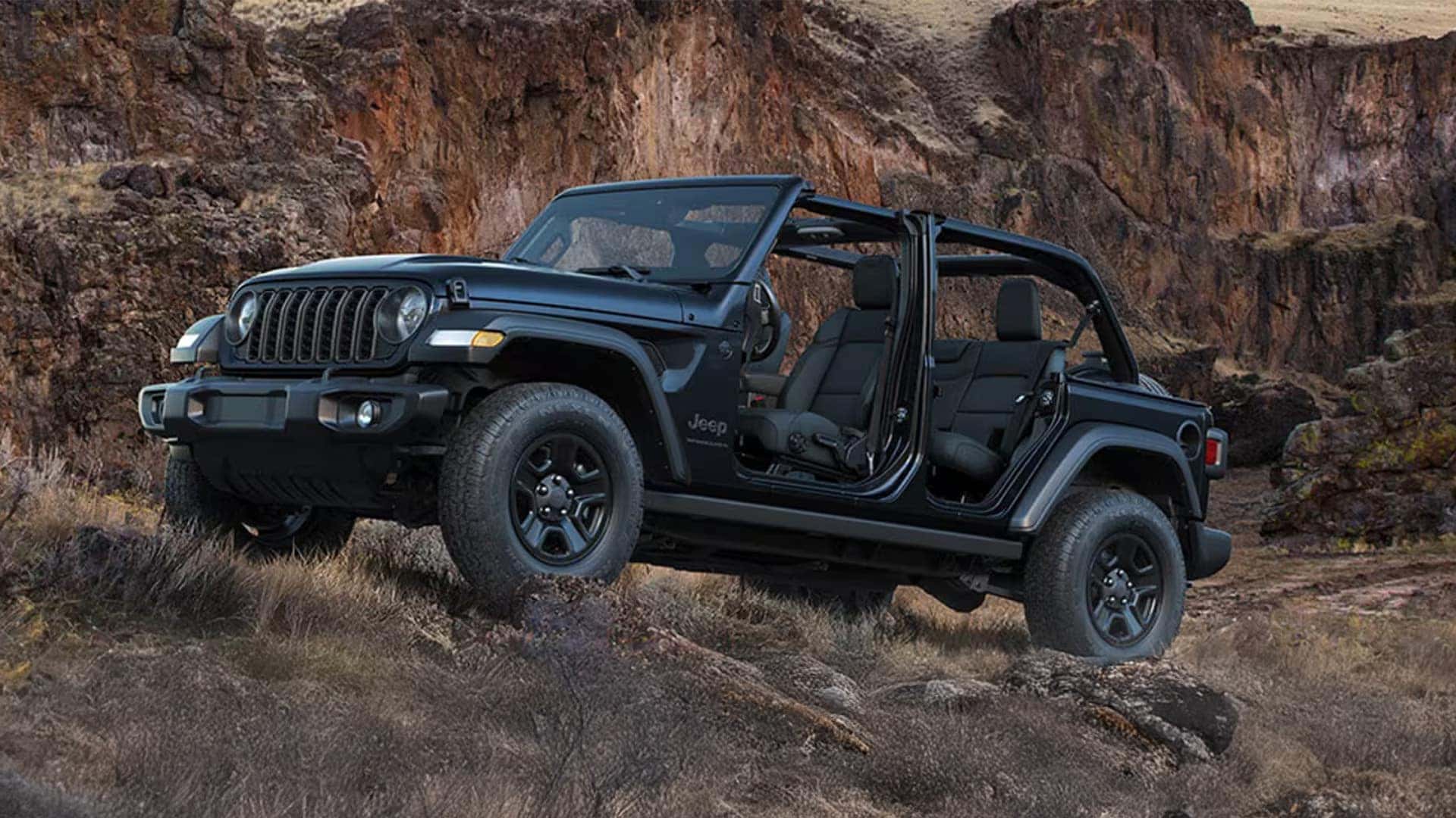 Black 2026 Jeep Wrangler with roof open and doors removed, parked on rocky terrain near canyon cliffs.