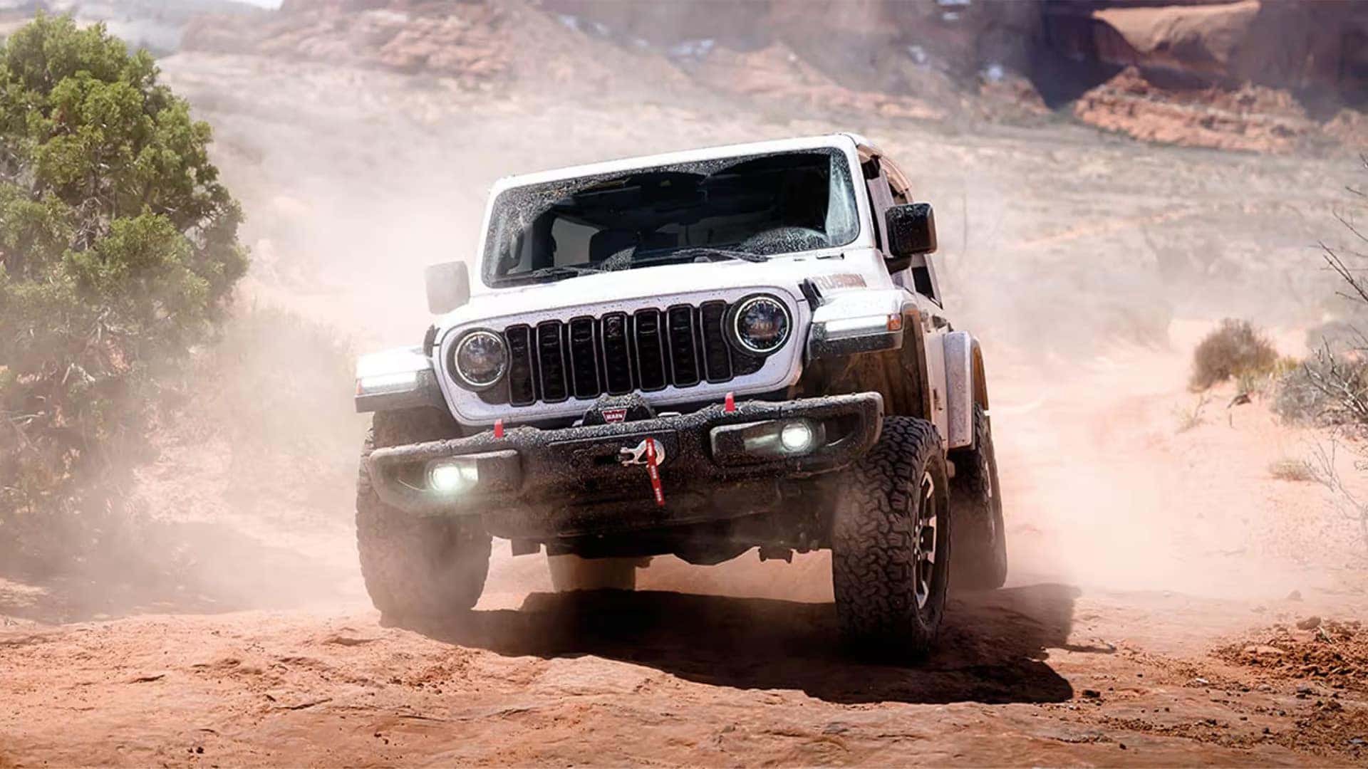 White 2026 Jeep Wrangler Rubicon driving on a dusty desert trail with off-road bumper and front winch
