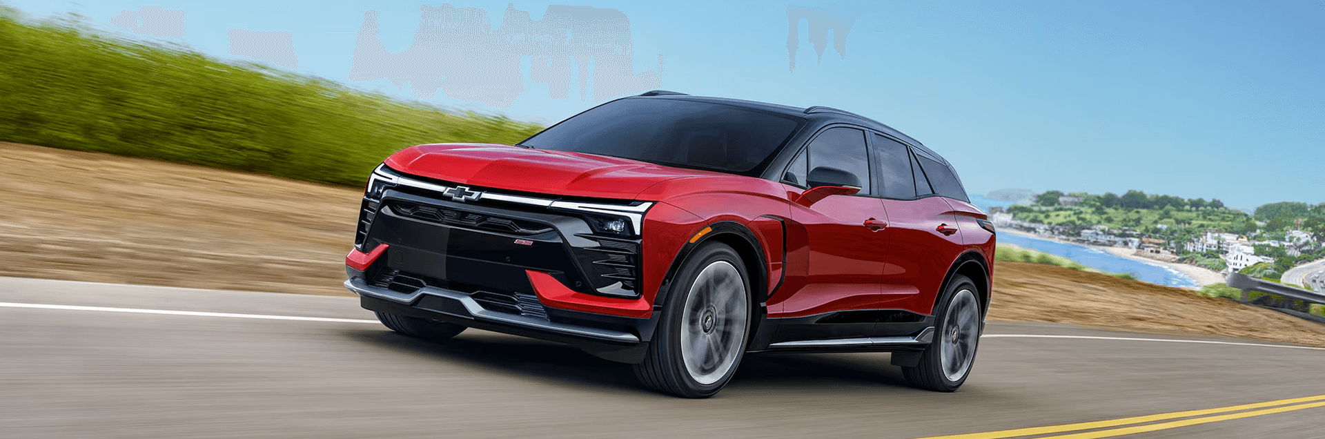 Red 2026 Chevy Blazer EV driving through a small town street with storefronts, showing side profile and motion blur