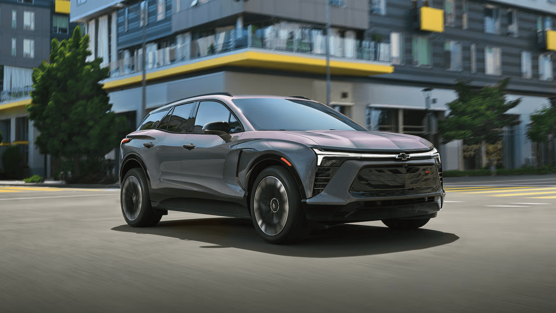 Gray Chevy Blazer EV driving through a city street, front three quarter view with LED light bar.