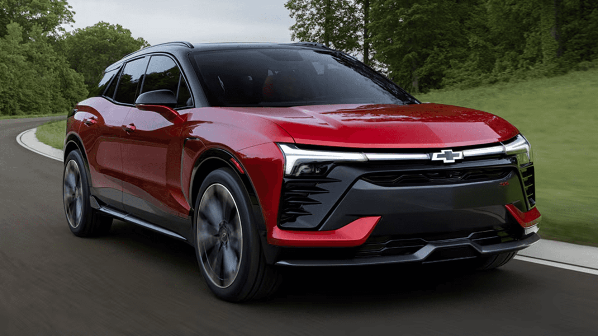 Red Chevy Blazer EV driving on a curving road, highlighting the full-width LED signature lighting.