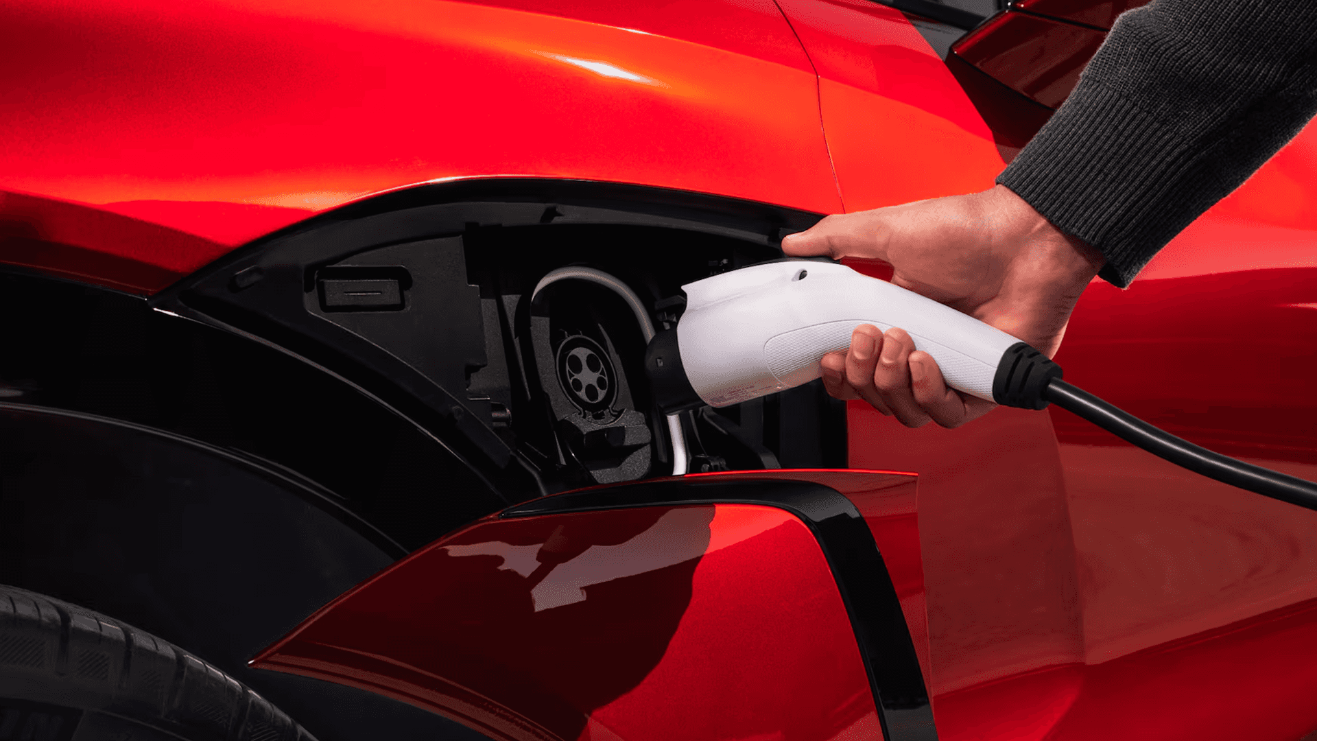 Close-up of a charging connector plugged into a red Chevy Blazer EV charge port behind the fender door.