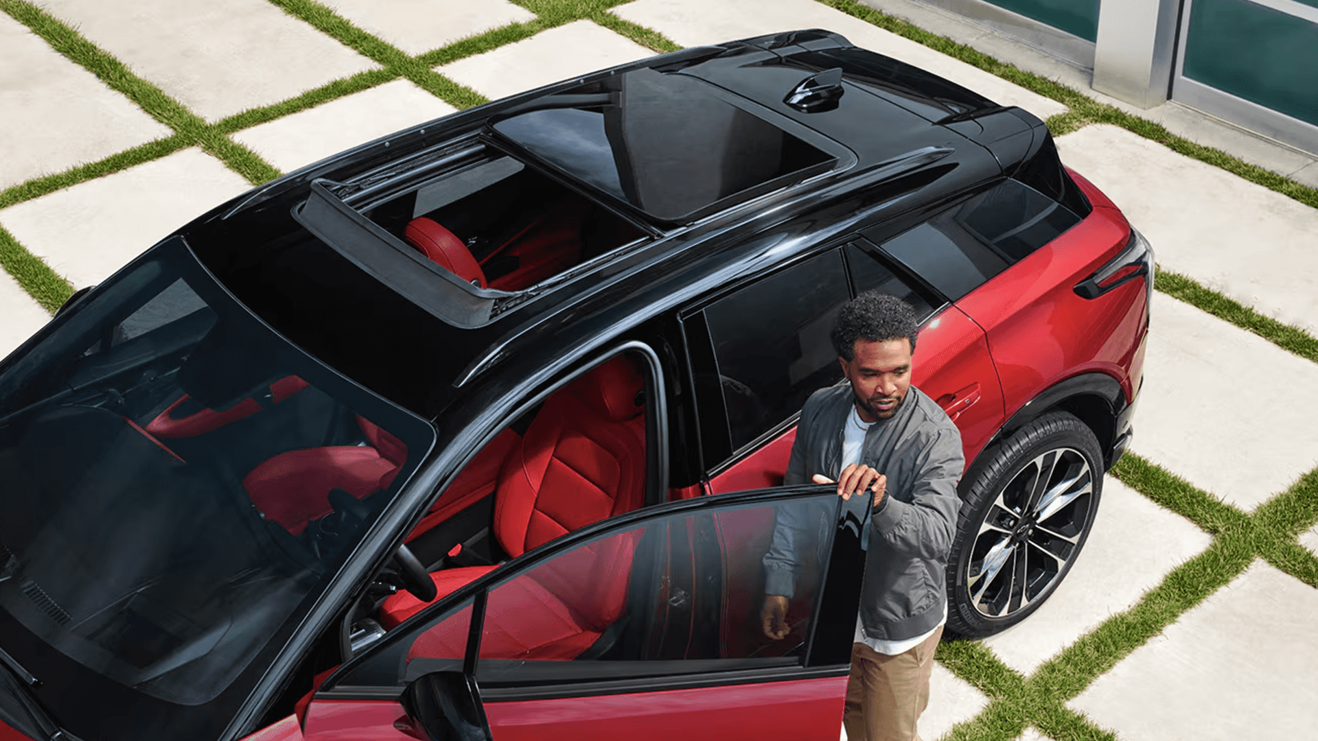 Overhead view of red Blazer EV with panoramic sunroof open as driver steps out beside red interior seats.