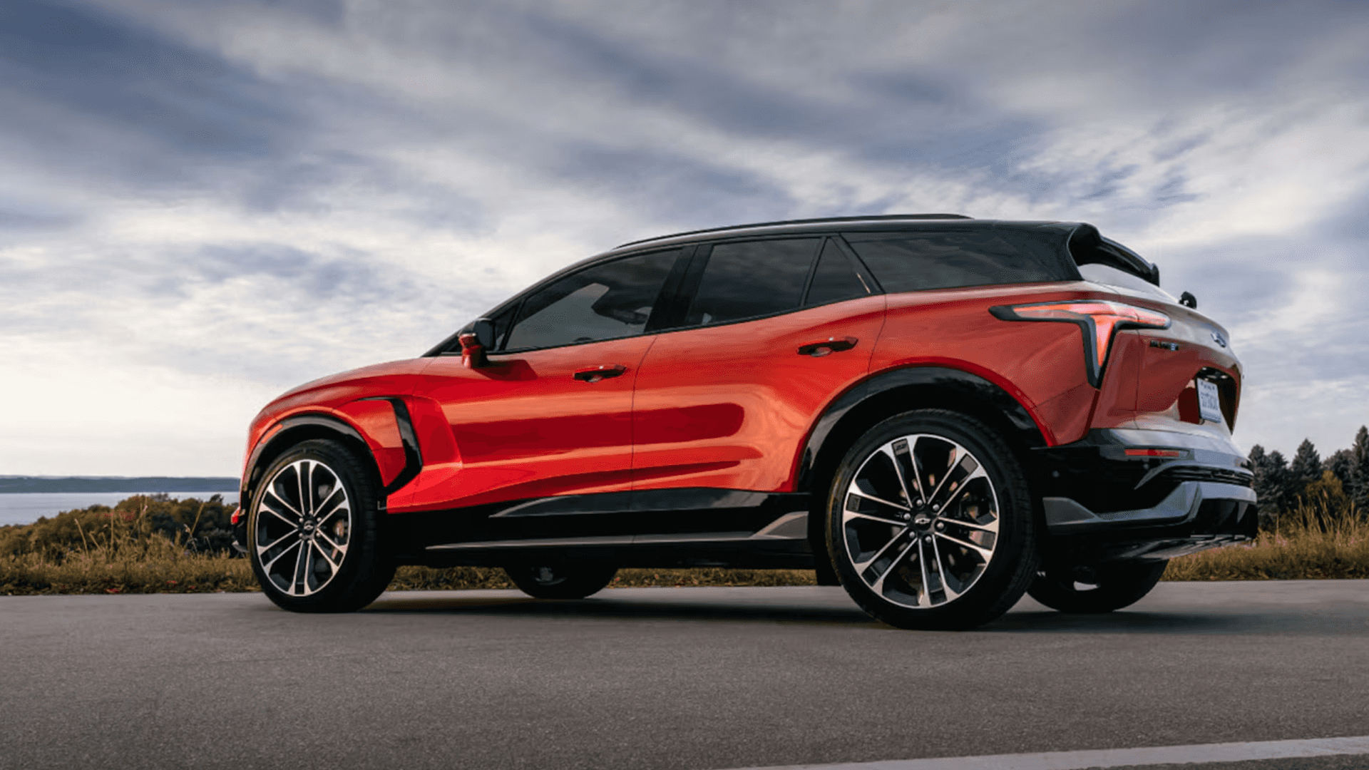 Red Chevy Blazer EV driving on open road, side profile with black roof, large alloy wheels, and LED lamps
