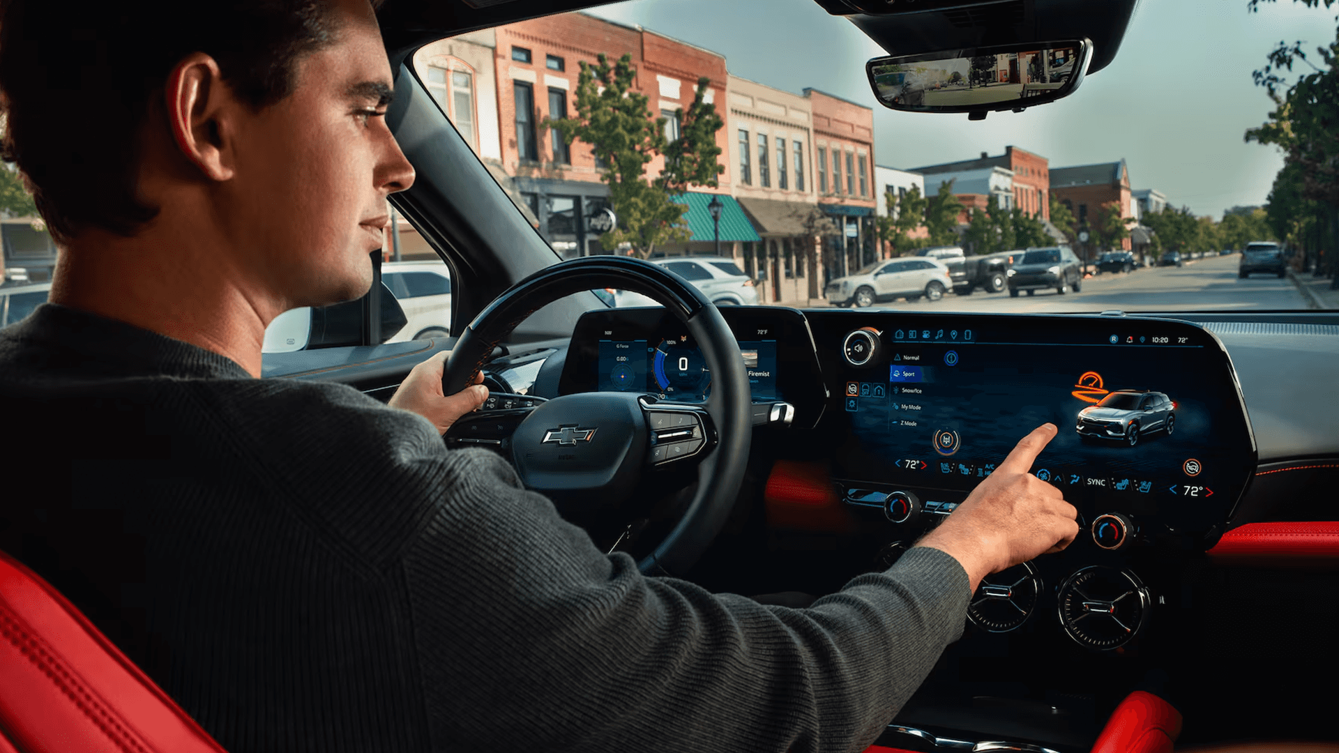 Driver taps wide infotainment touchscreen in Blazer EV cabin, with digital cluster and city street ahead