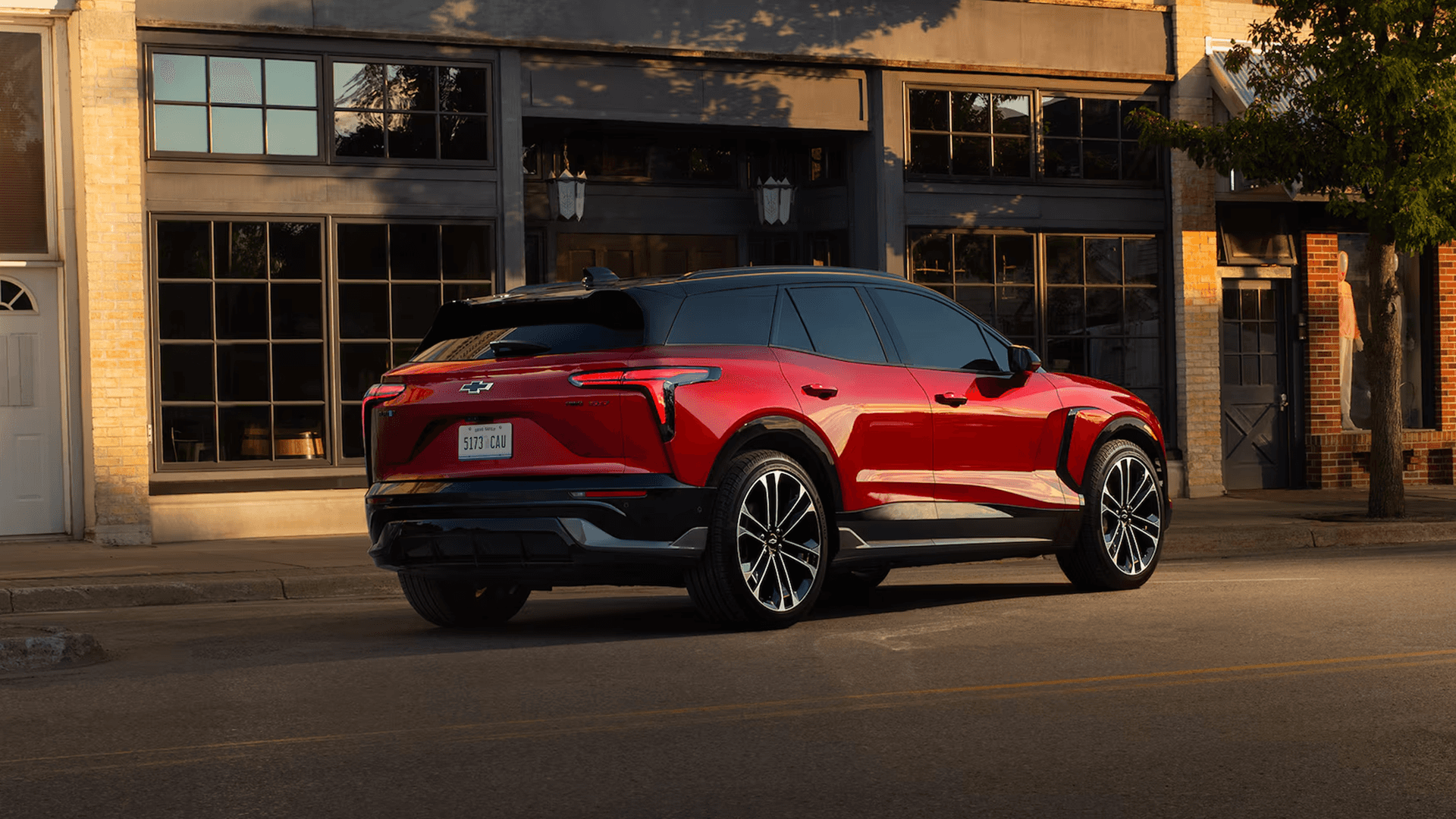 Rear three quarter view of red Blazer EV parked on main street, full width taillamps and black roof