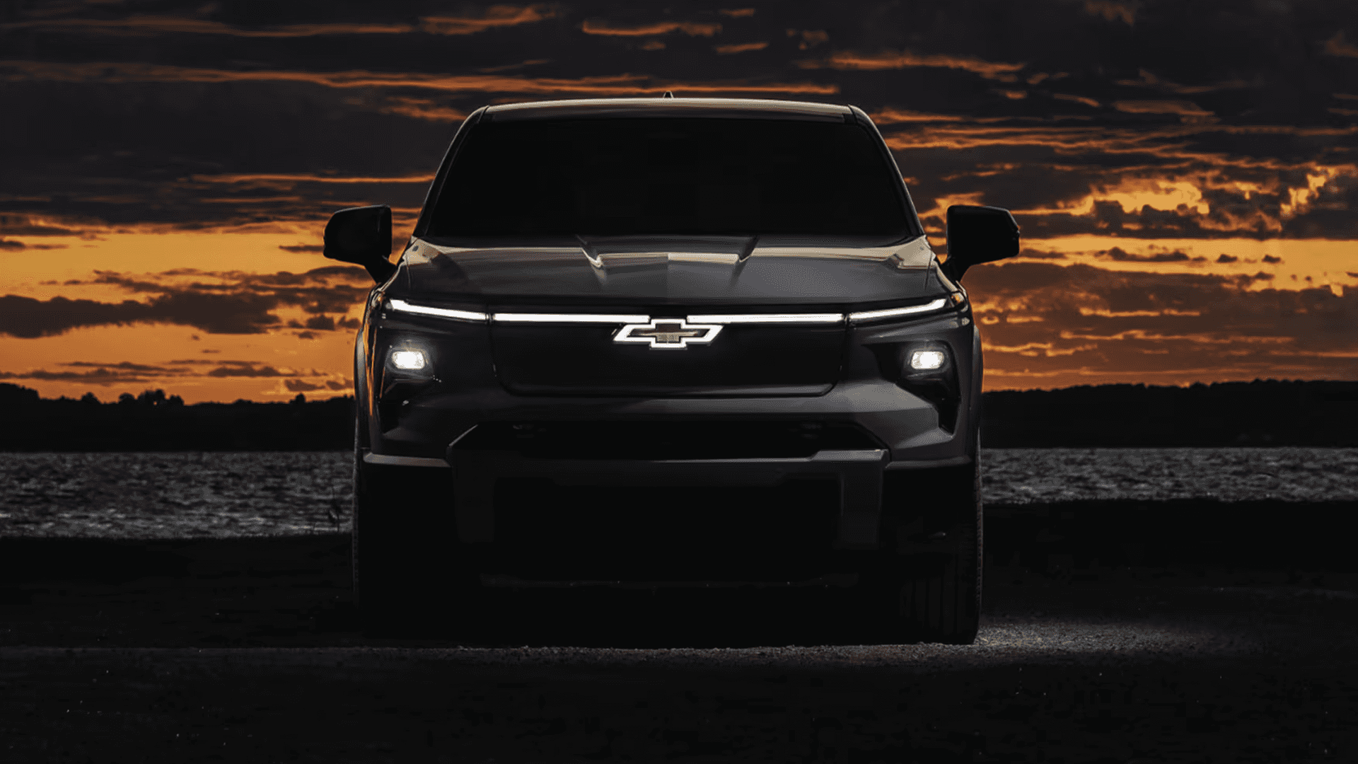 Front view of a Chevy Silverado EV at sunset showing the full LED light bar and illuminated bowtie emblem.